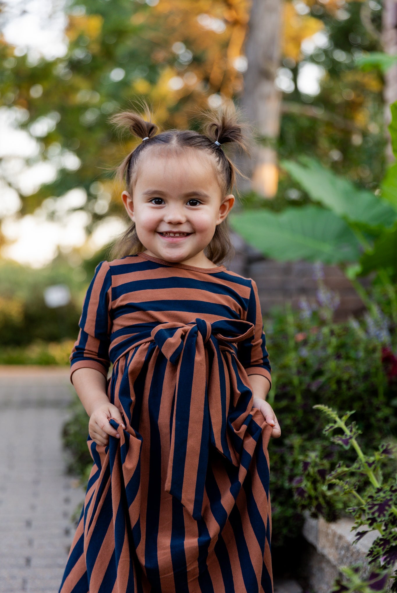 Young girl wearing the Nuggles® Girls Adelia Dress — a modest striped maxi dress with bow tie waist.