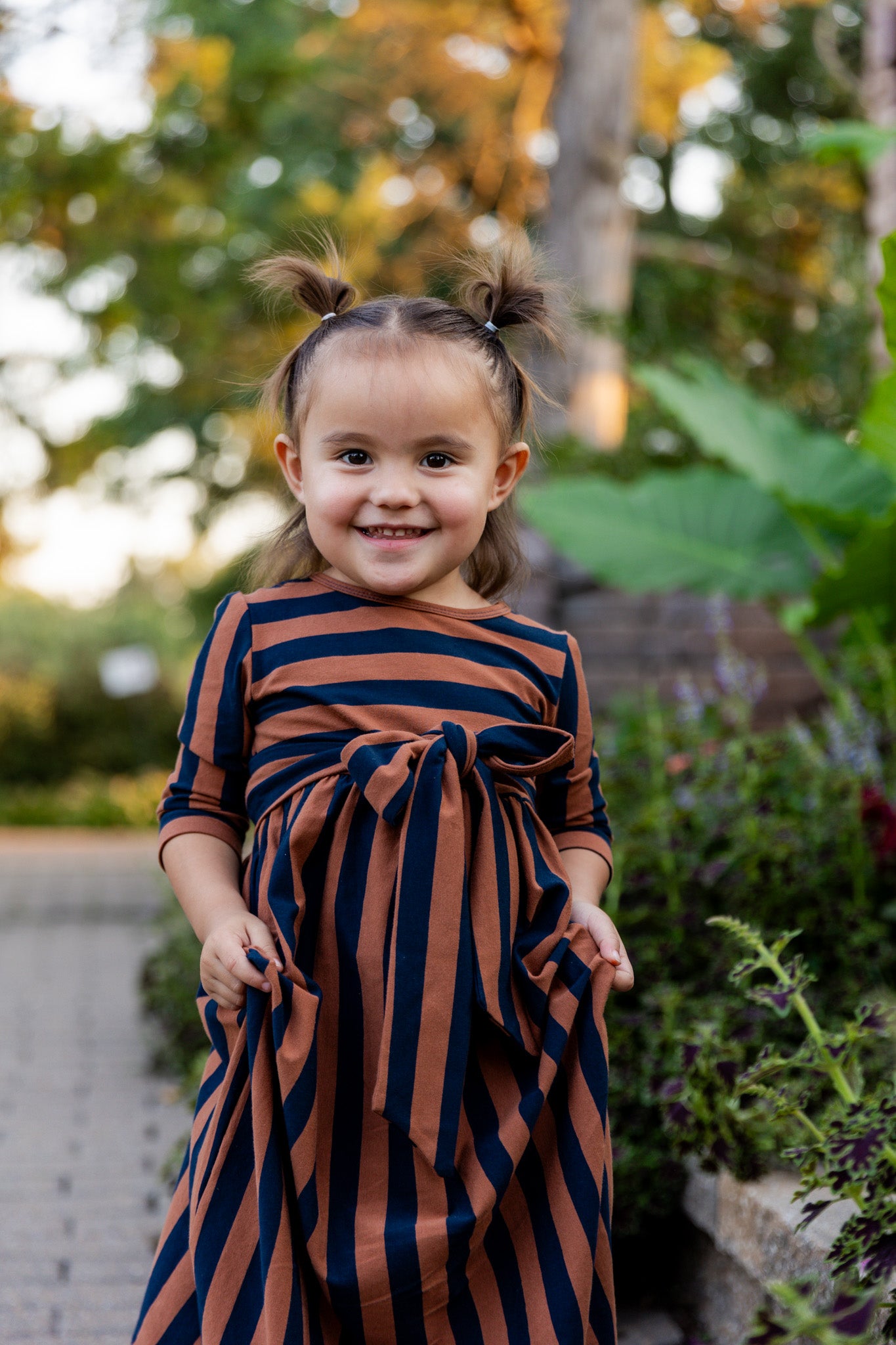 Young girl wearing the Nuggles® Girls Adelia Dress — a modest striped maxi dress with bow tie waist.