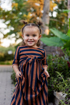 Young girl wearing the Nuggles® Girls Adelia Dress — a modest striped maxi dress with bow tie waist.