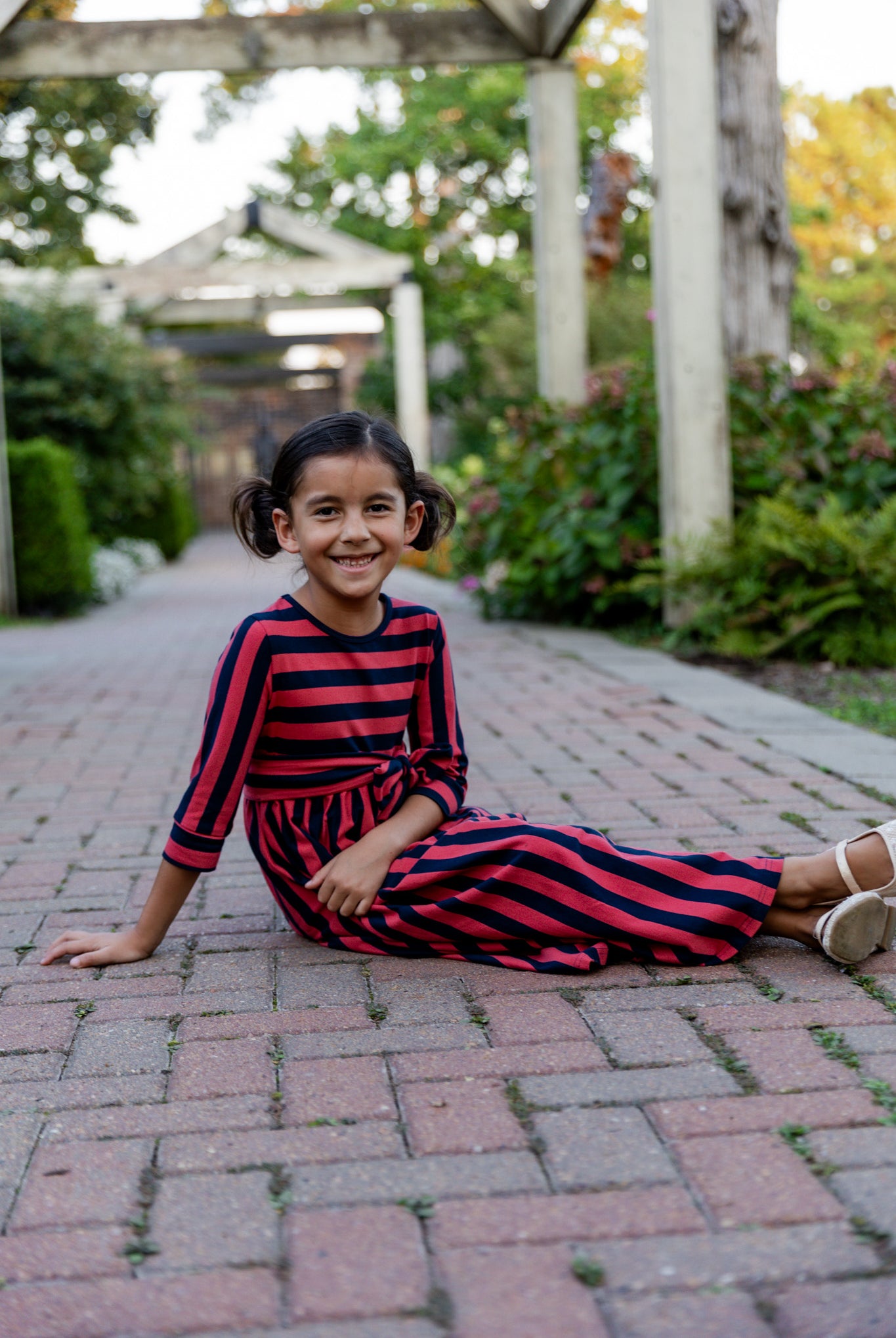 Young girl wearing the Nuggles® Girls Adelia Dress — a modest striped maxi dress with bow tie waist.