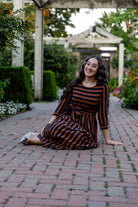 Model wearing the Nuggles® Adelia Dress, a modest striped maxi dress with waist tie and ¾ sleeves.