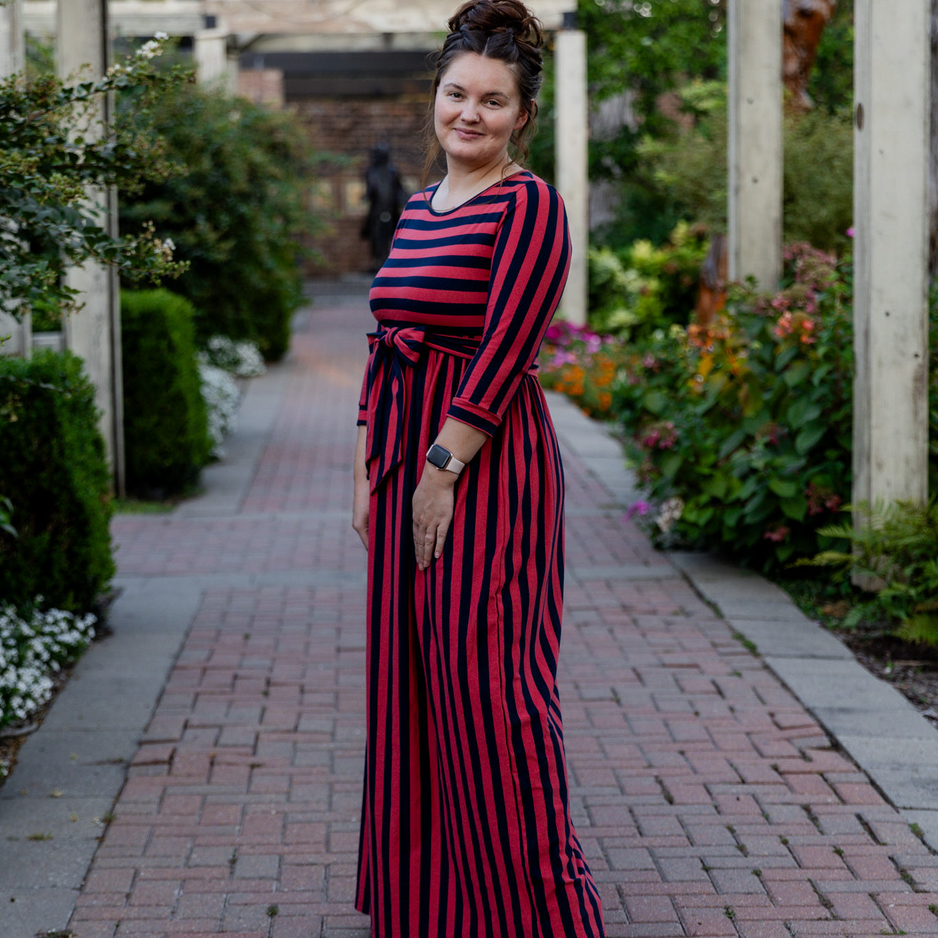 Model wearing the Nuggles® Adelia Dress, a modest striped maxi dress with waist tie and ¾ sleeves.