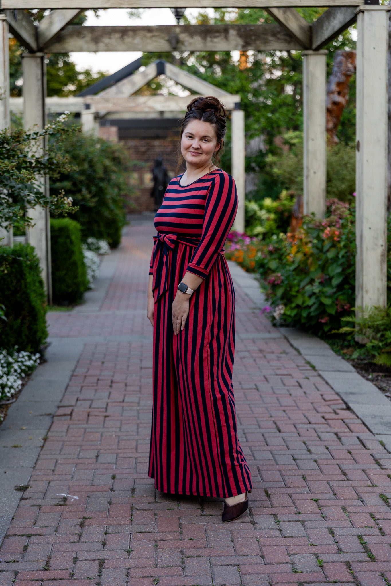 Model wearing the Nuggles® Adelia Dress, a modest striped maxi dress with waist tie and ¾ sleeves.
