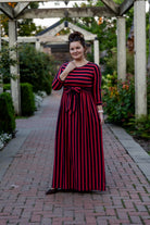 Model wearing the Nuggles® Adelia Dress, a modest striped maxi dress with waist tie and ¾ sleeves.