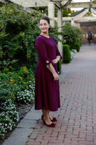 Model wearing the Nuggles® Gracie Dress, a modest A-line midi dress with ¾ sleeves and tie accents, made from soft knit fabric.