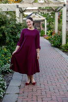 Model wearing the Nuggles® Gracie Dress, a modest A-line midi dress with ¾ sleeves and tie accents, made from soft knit fabric.