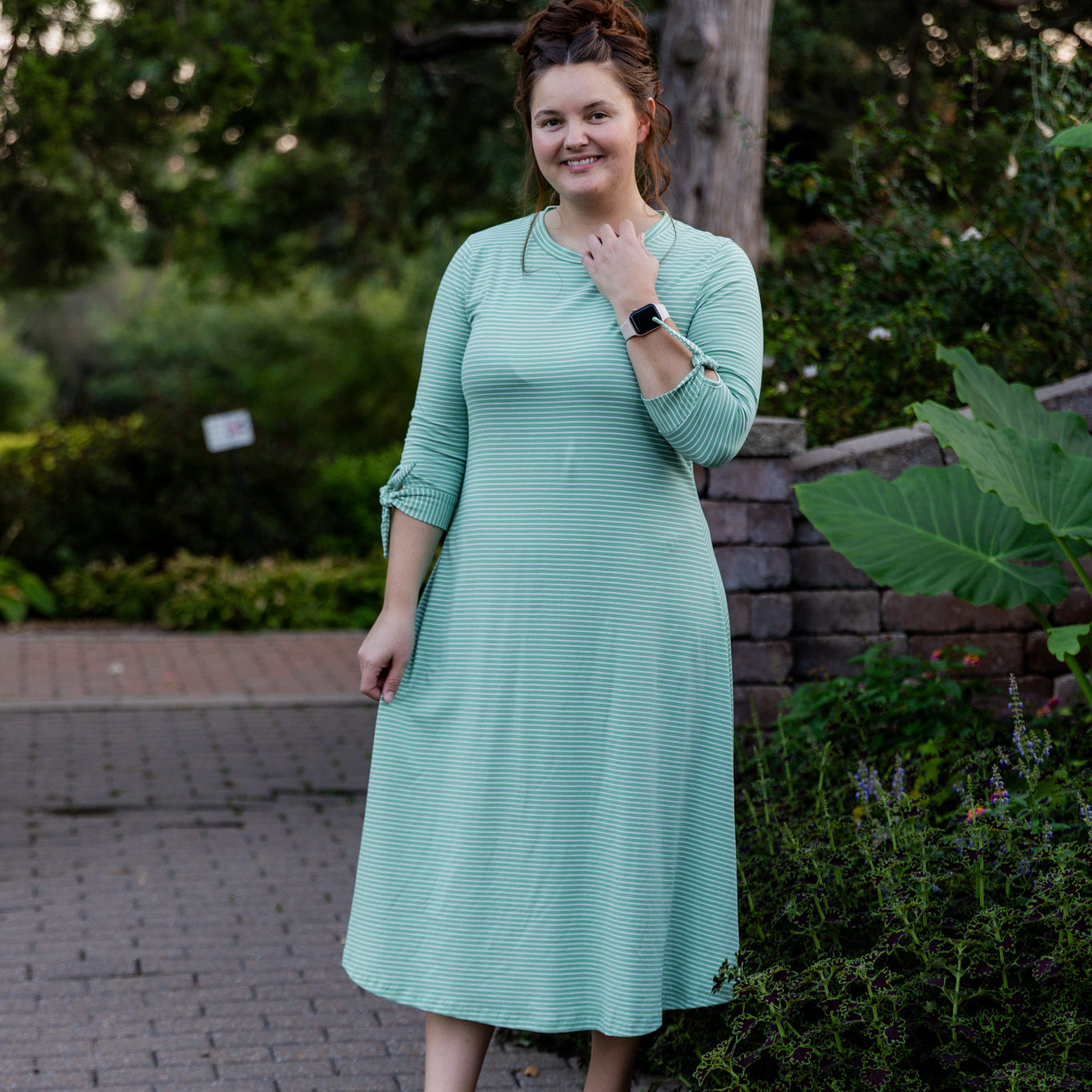 Model wearing the Nuggles® Gracie Dress, a modest A-line midi dress with ¾ sleeves and tie accents, made from soft knit fabric.