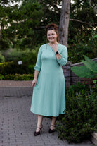 Model wearing the Nuggles® Gracie Dress, a modest A-line midi dress with ¾ sleeves and tie accents, made from soft knit fabric.