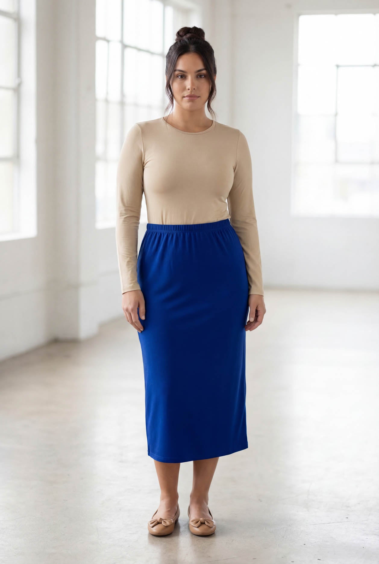 Woman wearing a beige top and blue skirt in a bright room