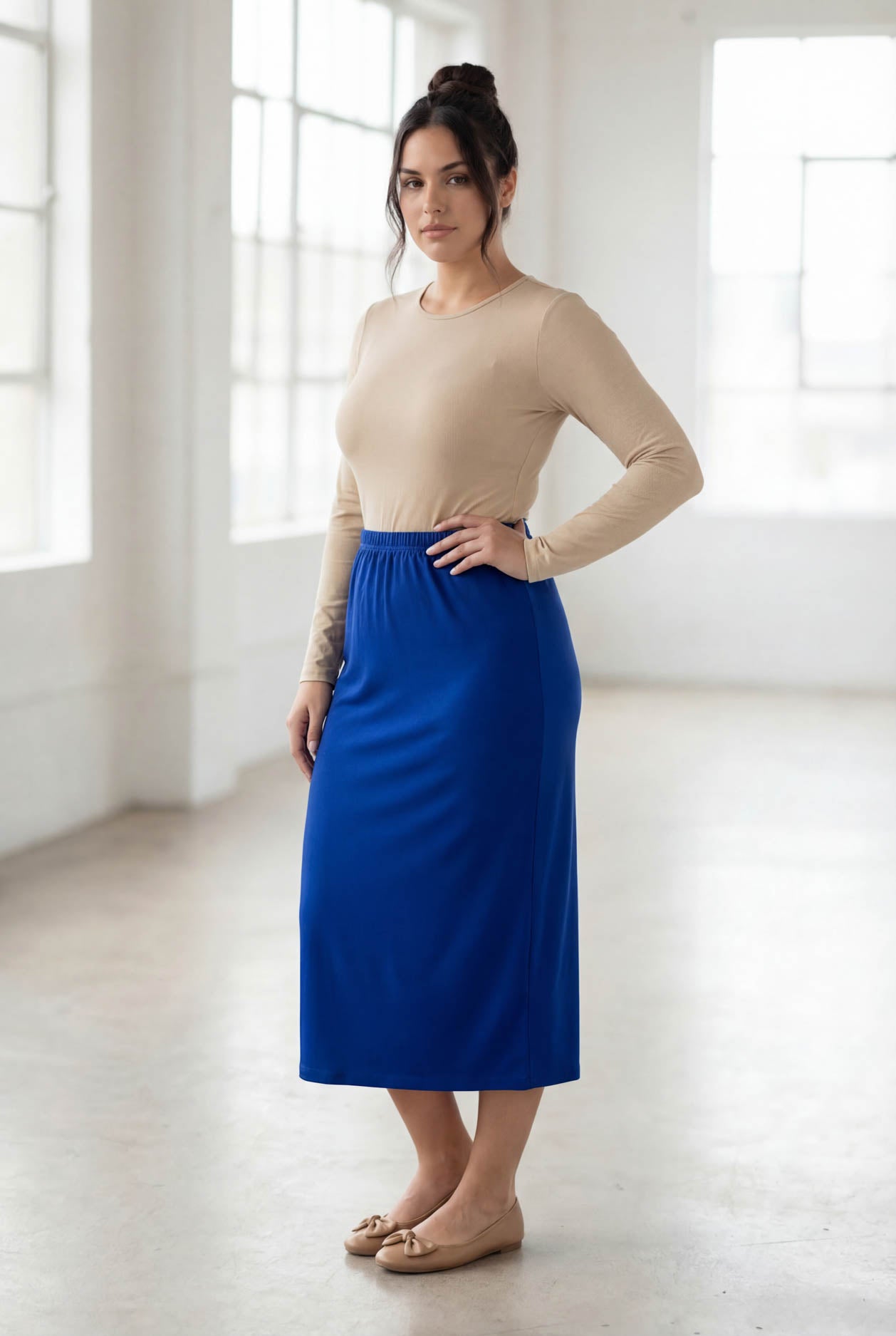 Woman wearing a beige top and blue skirt in a bright room.