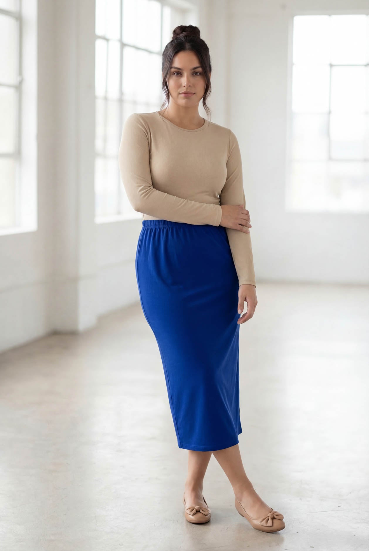 Woman wearing a beige top and blue skirt in a bright room