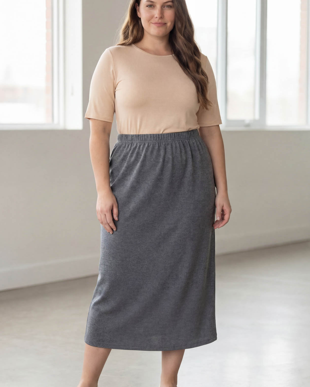 Woman wearing a beige top and gray skirt in a bright room.