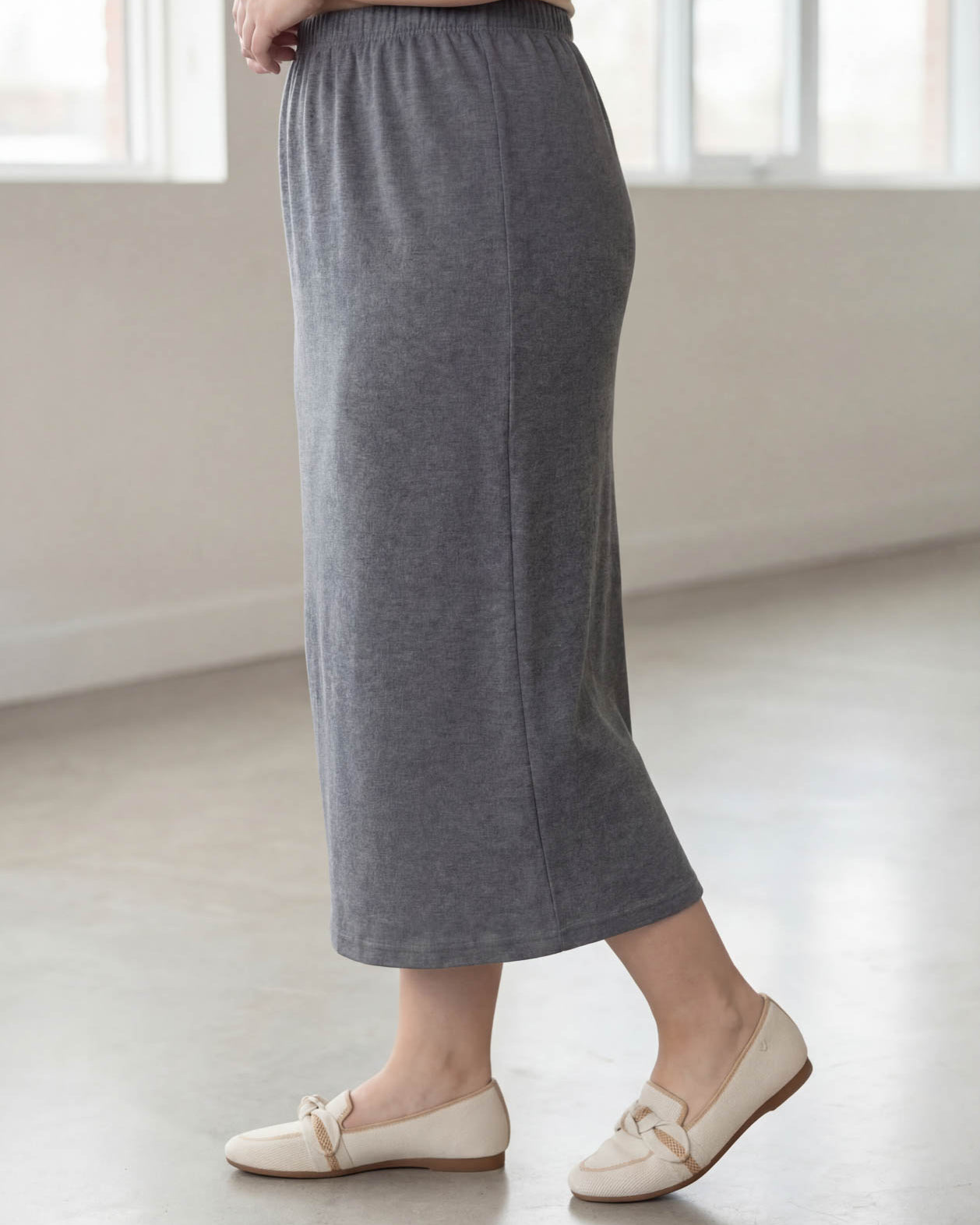 Woman wearing a beige top and gray skirt in a bright room.