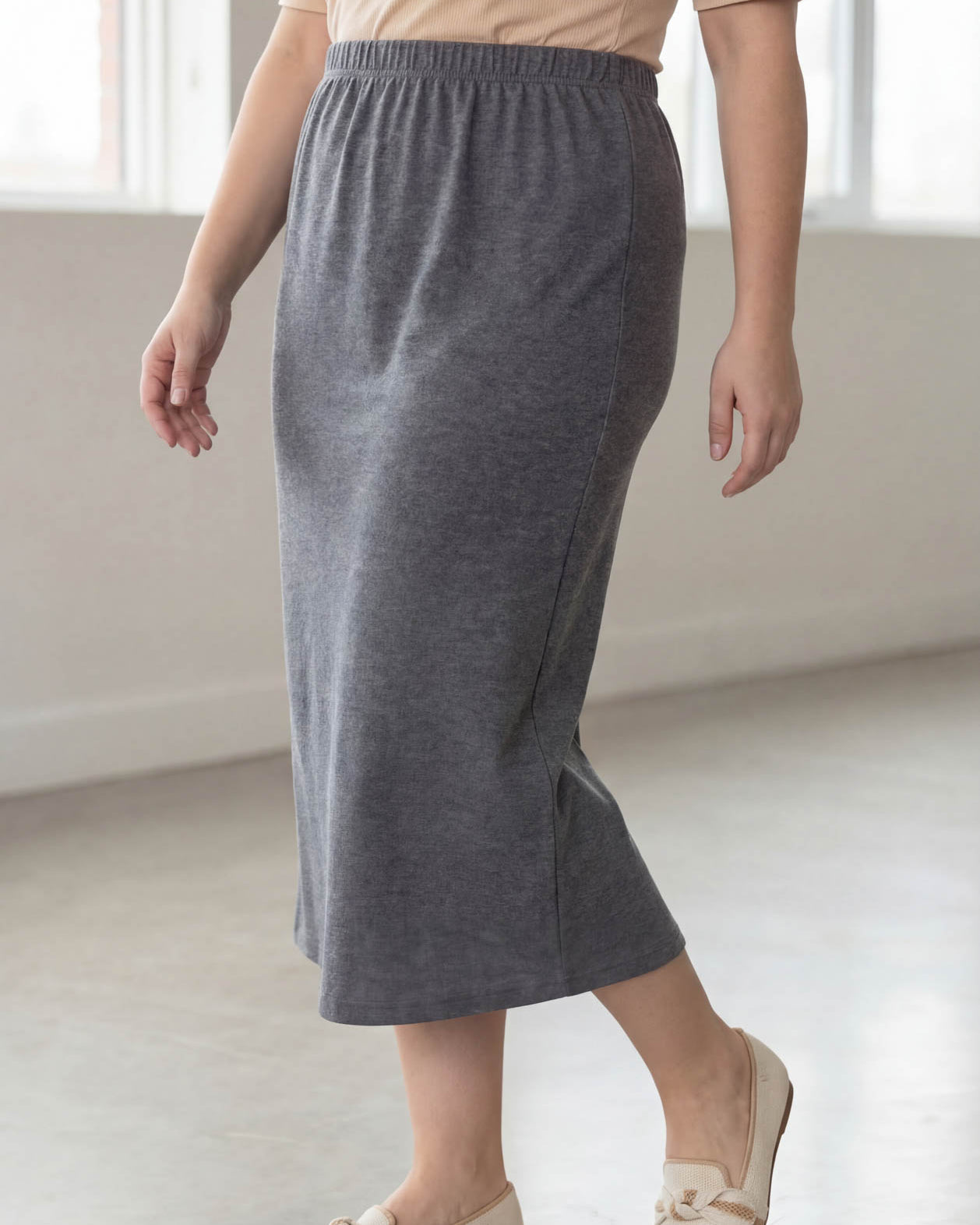 Woman wearing a beige top and gray skirt in a bright room.