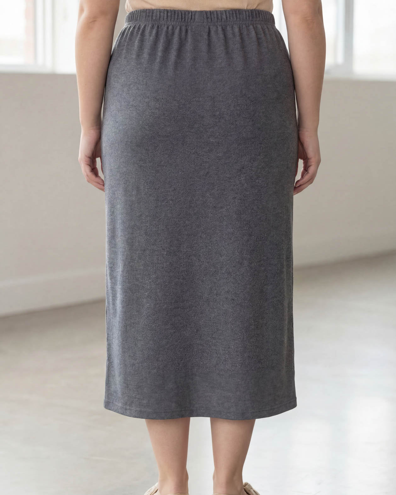 Woman wearing a beige top and gray skirt in a bright room.