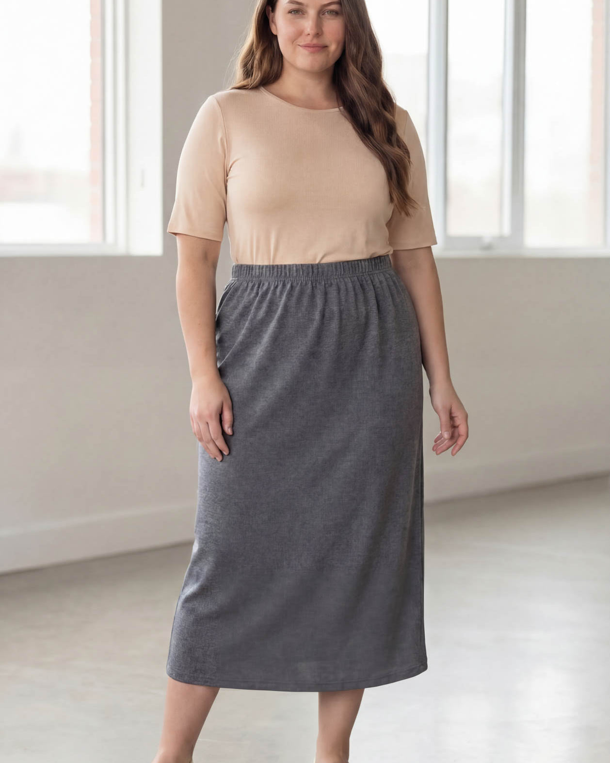 Woman wearing a beige top and gray skirt in a bright room.