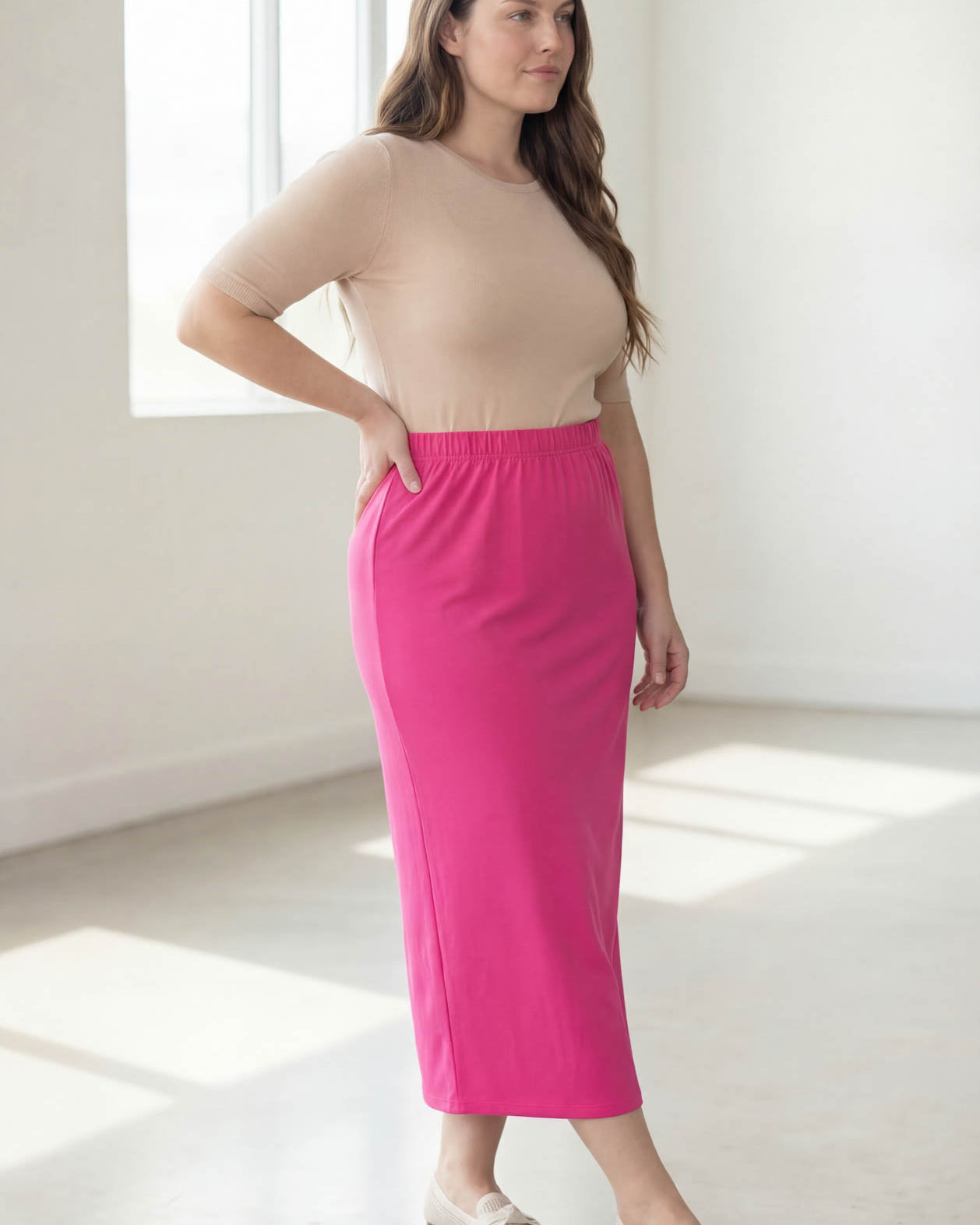 Woman wearing a beige top and pink skirt in a bright room.