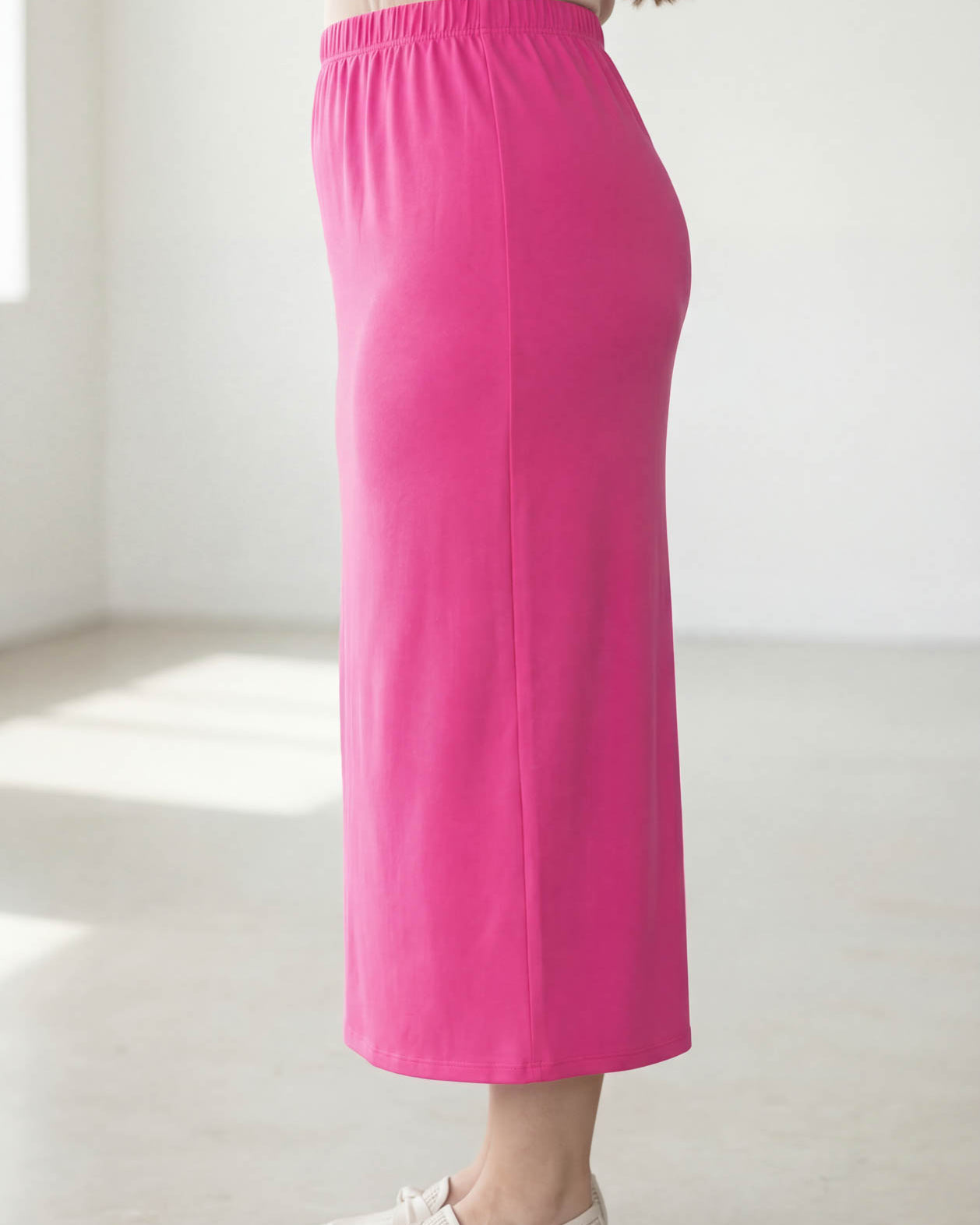 Woman wearing a beige top and pink skirt in a bright room.