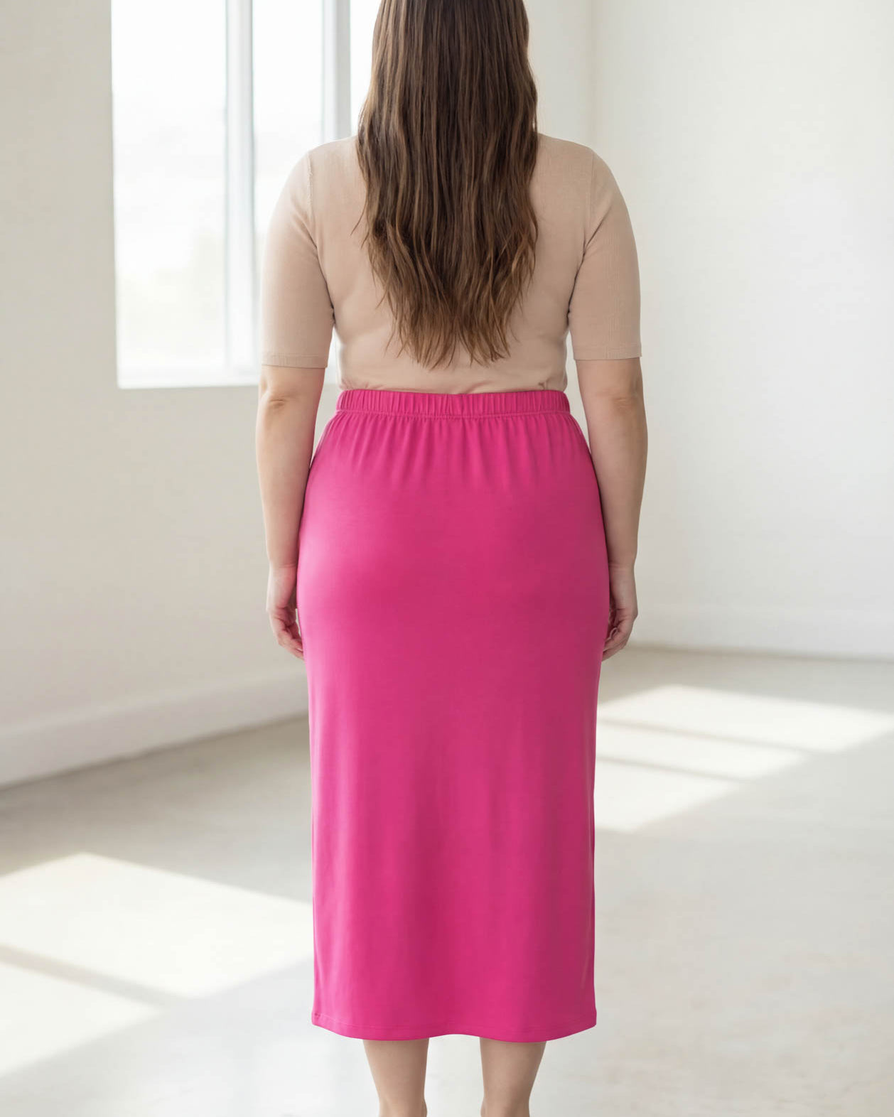 Woman wearing a beige top and pink skirt in a bright room.