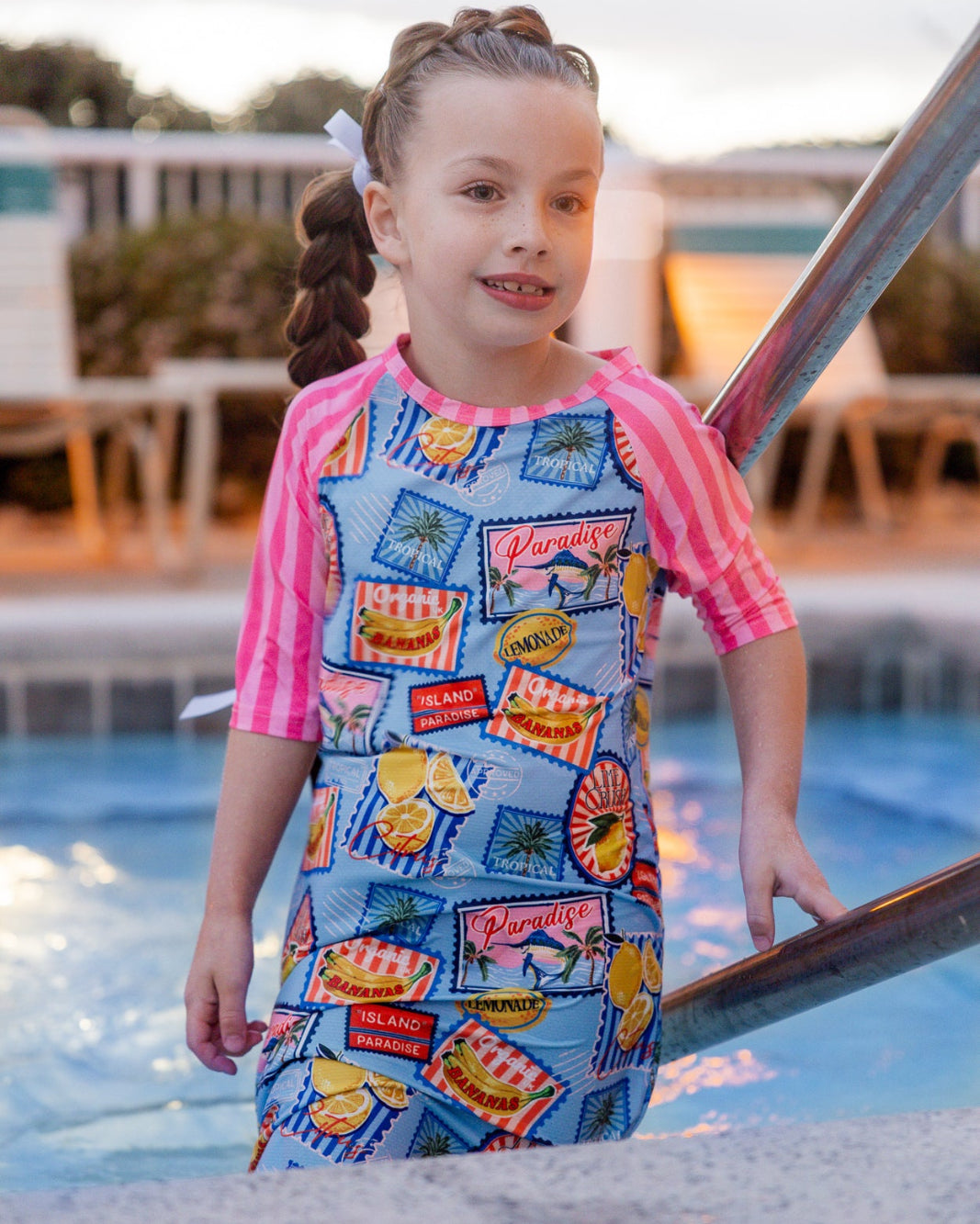 Model wearing Nuggles® Girls' Sport Swim Dress in Vacation Postcards