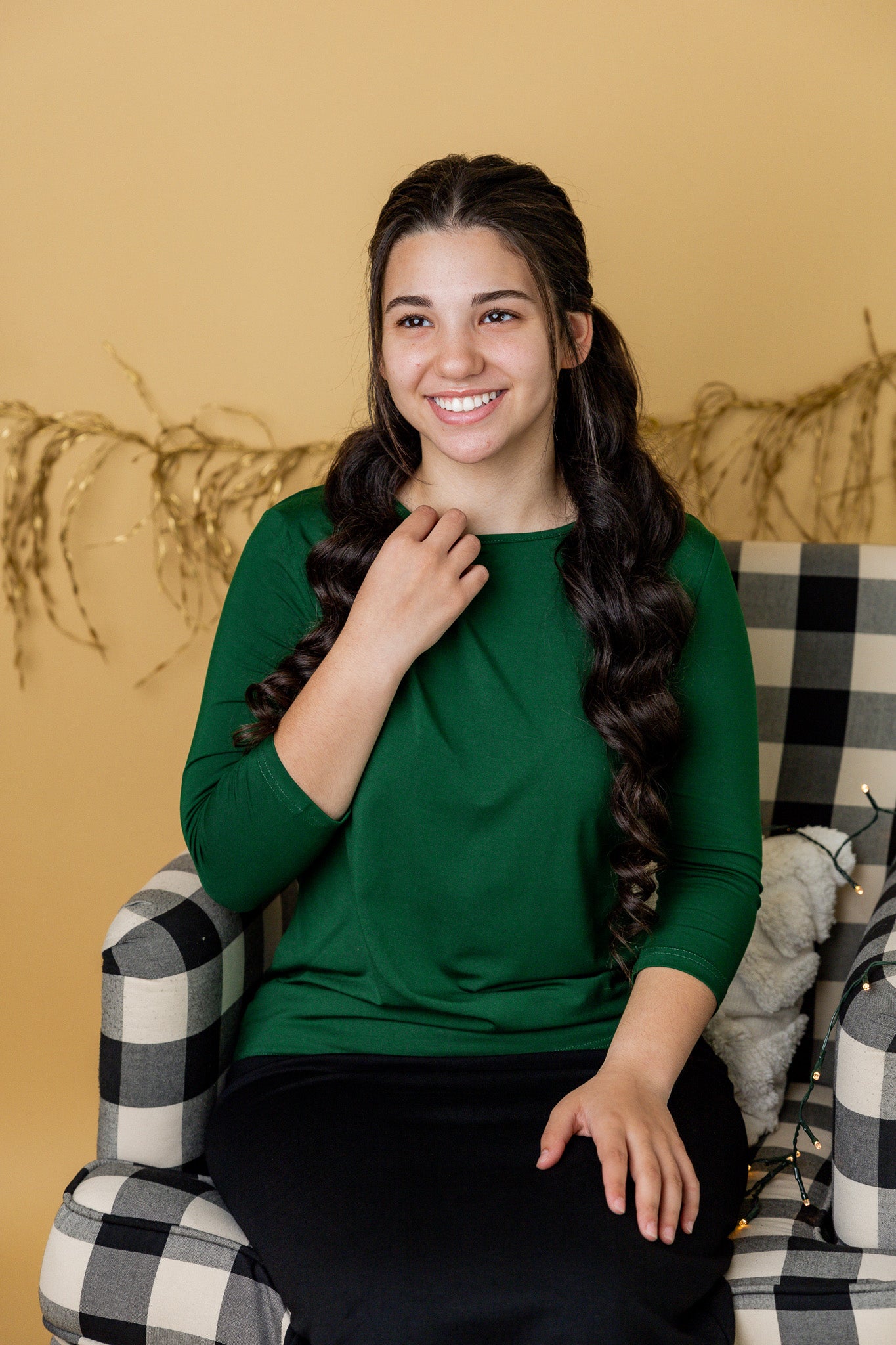 Woman in a green shirt sitting on a checkered chair against a beige wall.