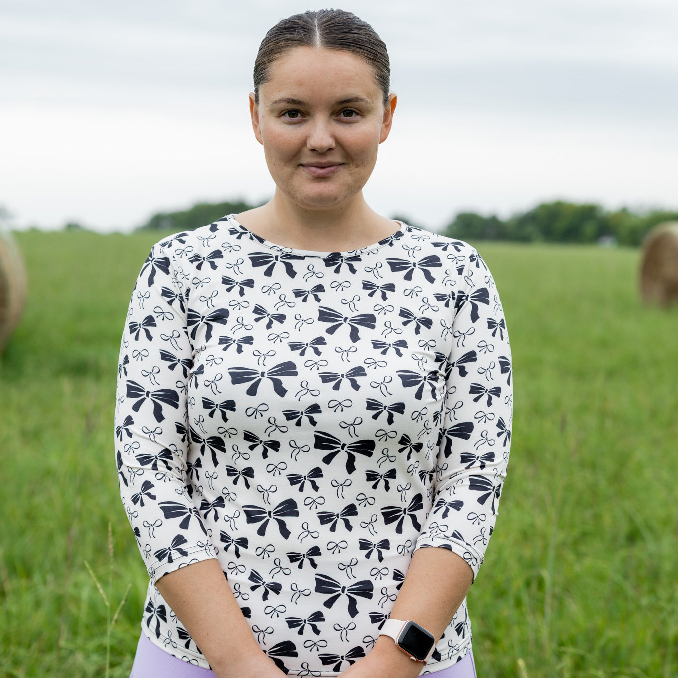 Woman standing in a field holding a basket of flowers, wearing a patterned shirt.