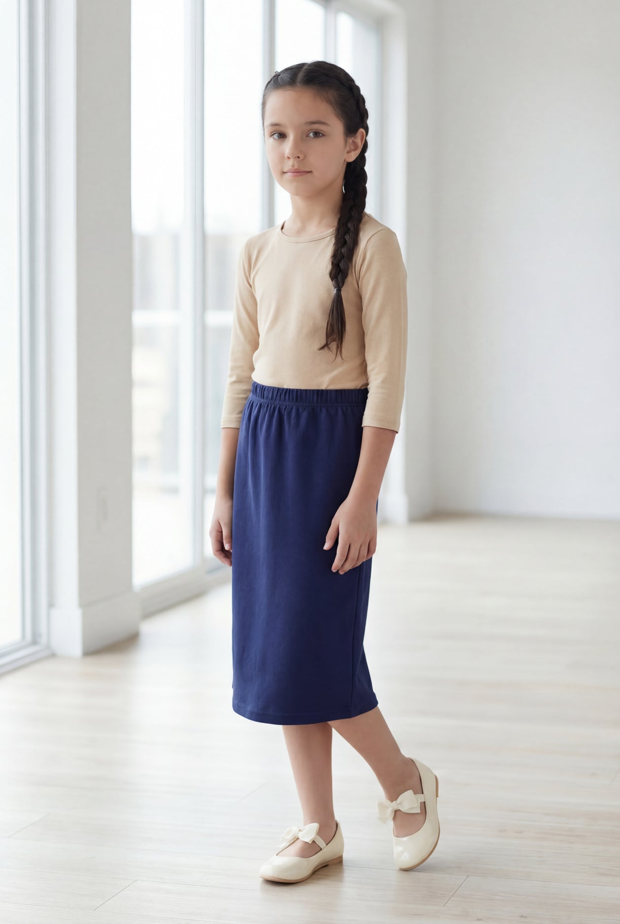 Young girl wearing a modest midi length skirt in navy with a beige colored 3/4 length sleeve shirt.