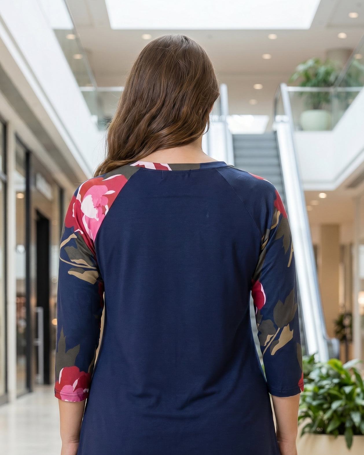 Woman modeling a navy floral-sleeve top in a mall.