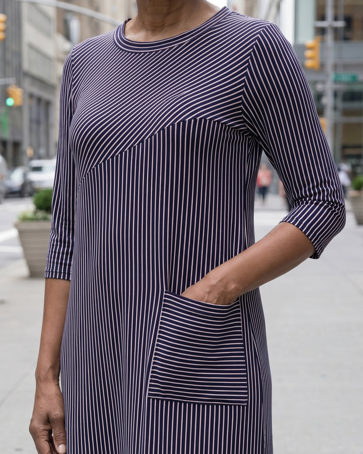 Women standing in a navy and pink stripe dress on a busy city street.