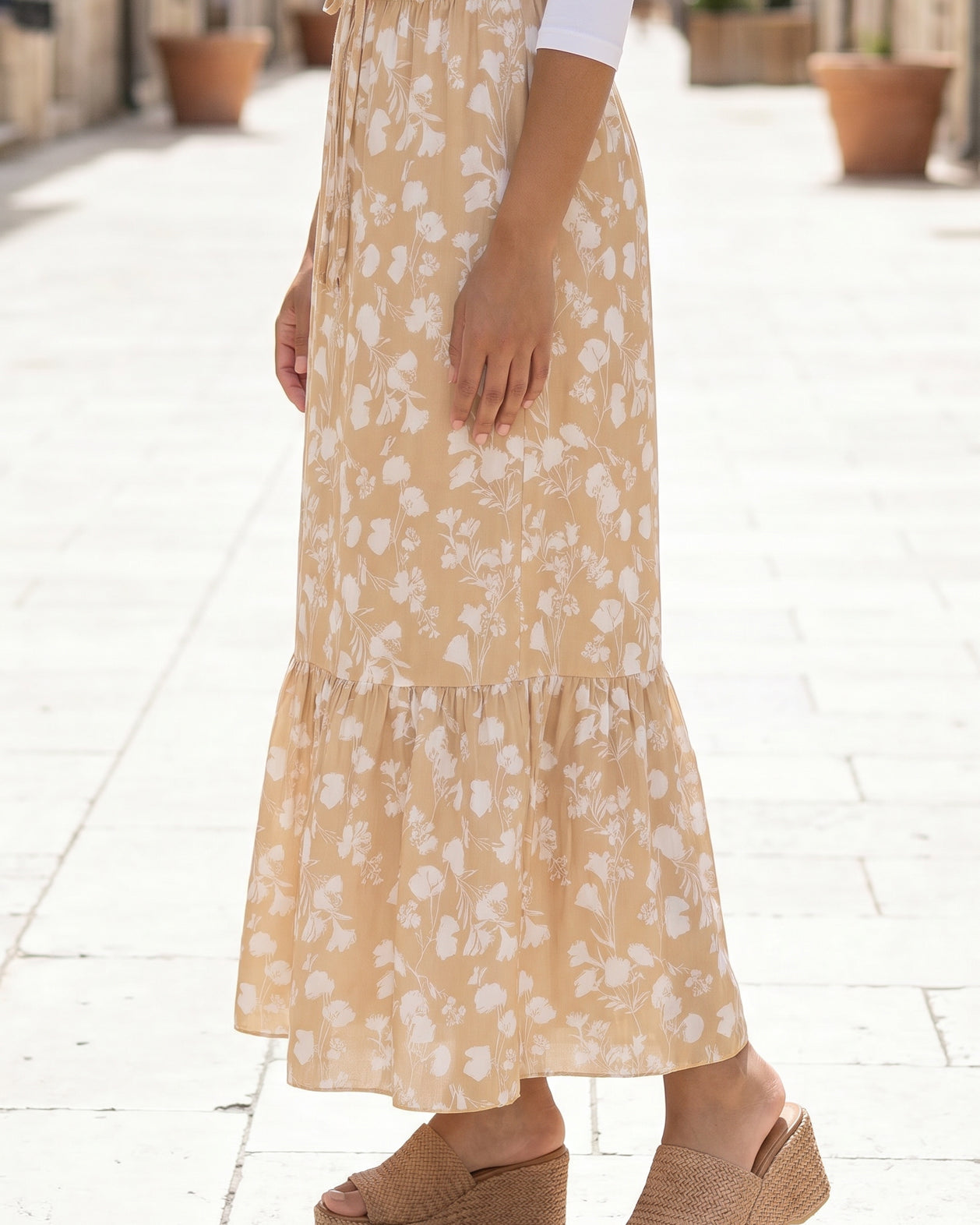 Woman in a white top and yellow floral skirt standing on a stone-paved street.