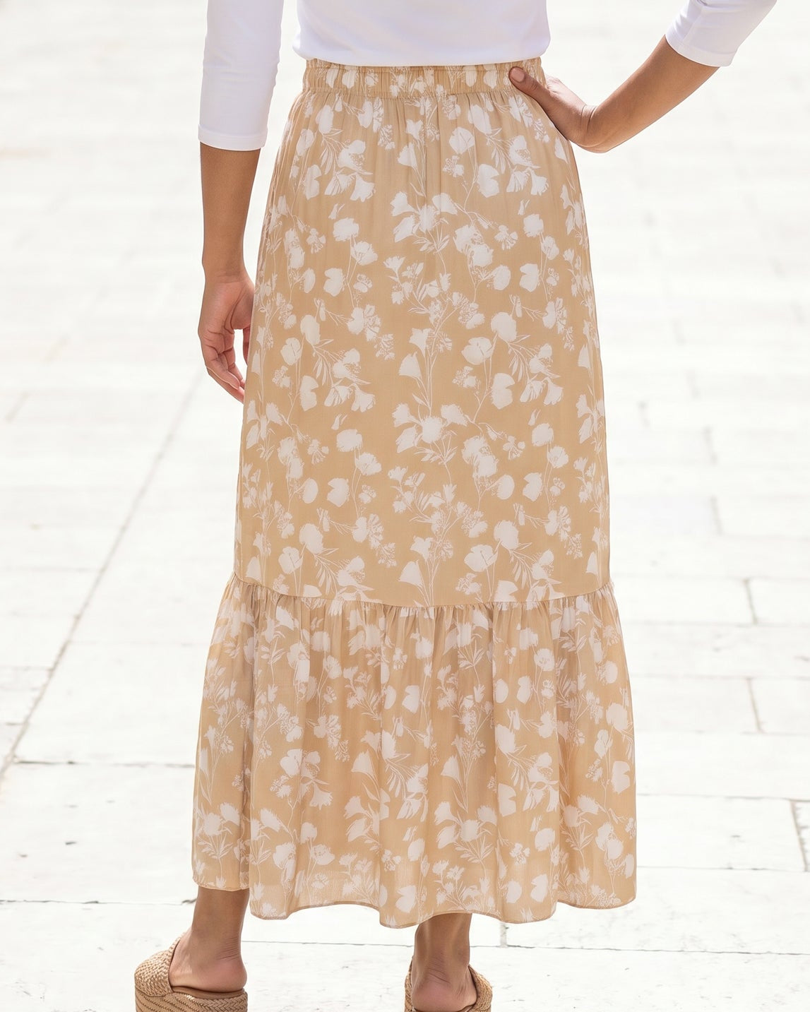 Woman in a white top and yellow floral skirt standing on a stone-paved street.
