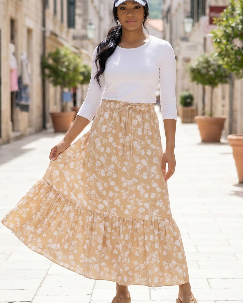 Woman in a white top and beige floral skirt standing on a stone-paved street.