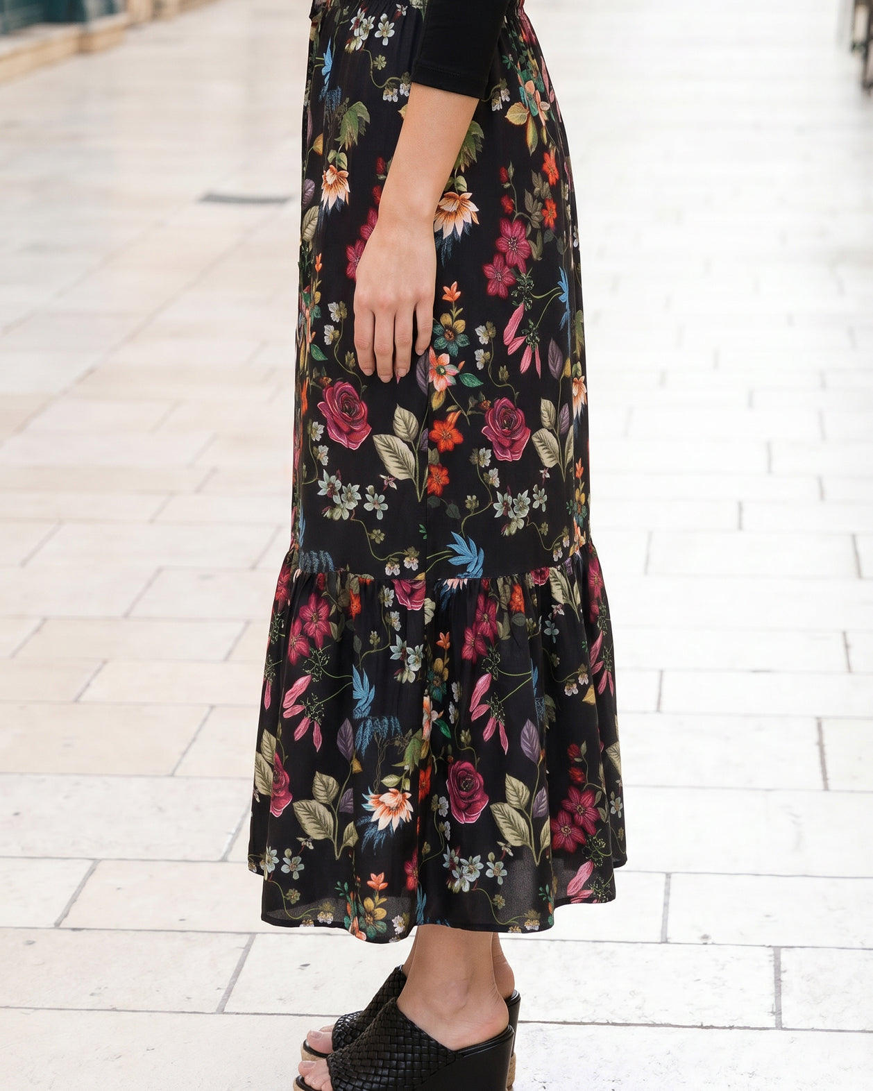 Person wearing a black floral skirt on a light stone pavement.
