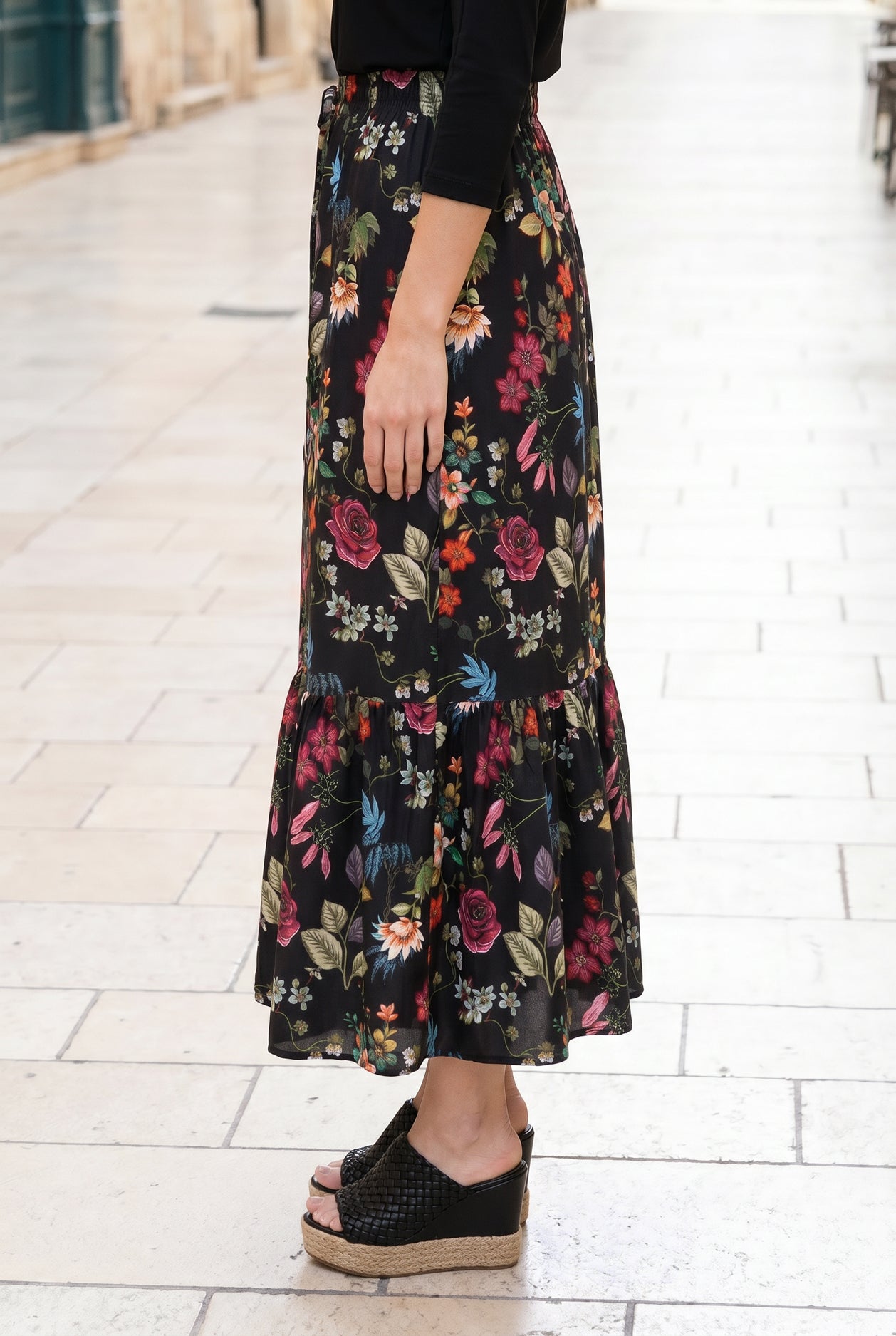 Person wearing a black floral skirt on a light stone pavement.