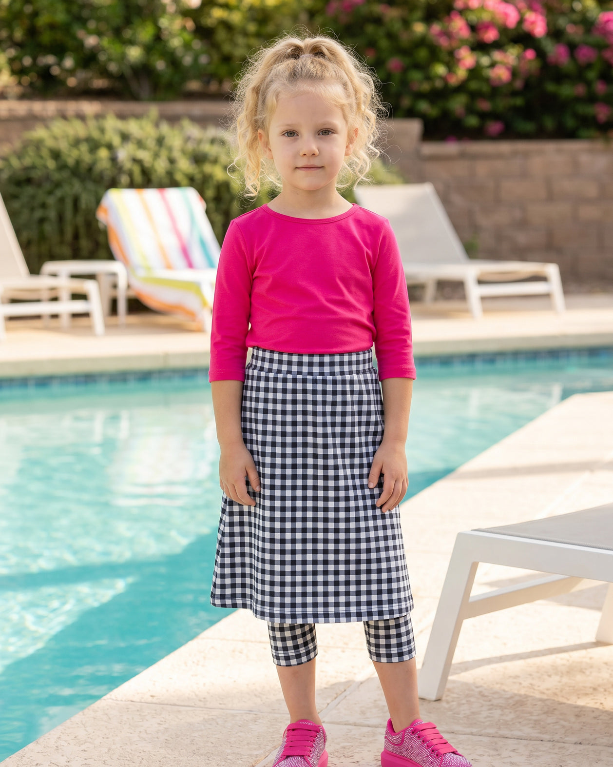 A picture of a young girl beside a pool with a beach ball wearing a modest skort with a coordinating hot pink shirt.