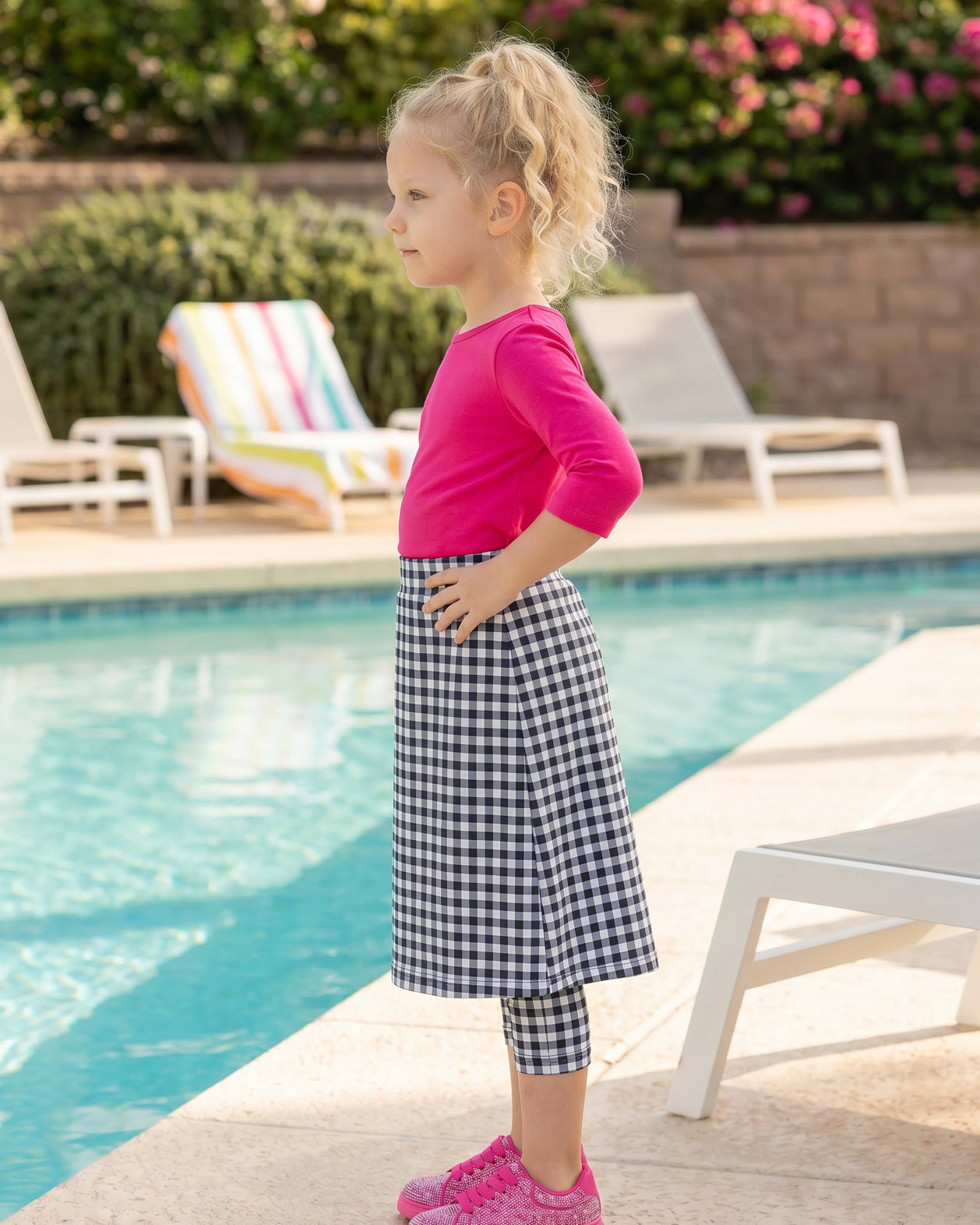 A picture of a young girl beside a pool with a beach ball wearing a modest skort with a coordinating hot pink shirt.