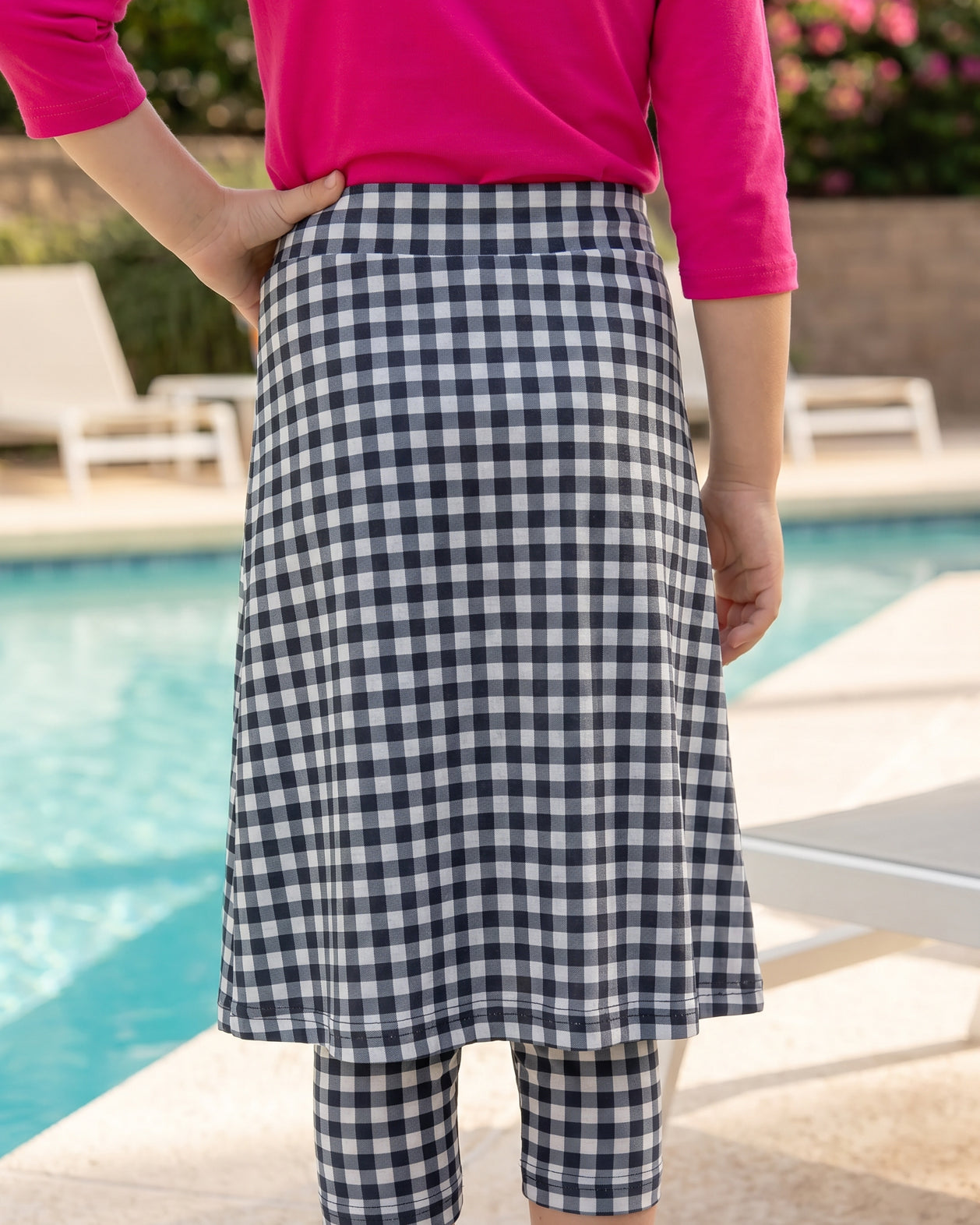A picture of a young girl beside a pool with a beach ball wearing a modest skort with a coordinating hot pink shirt.