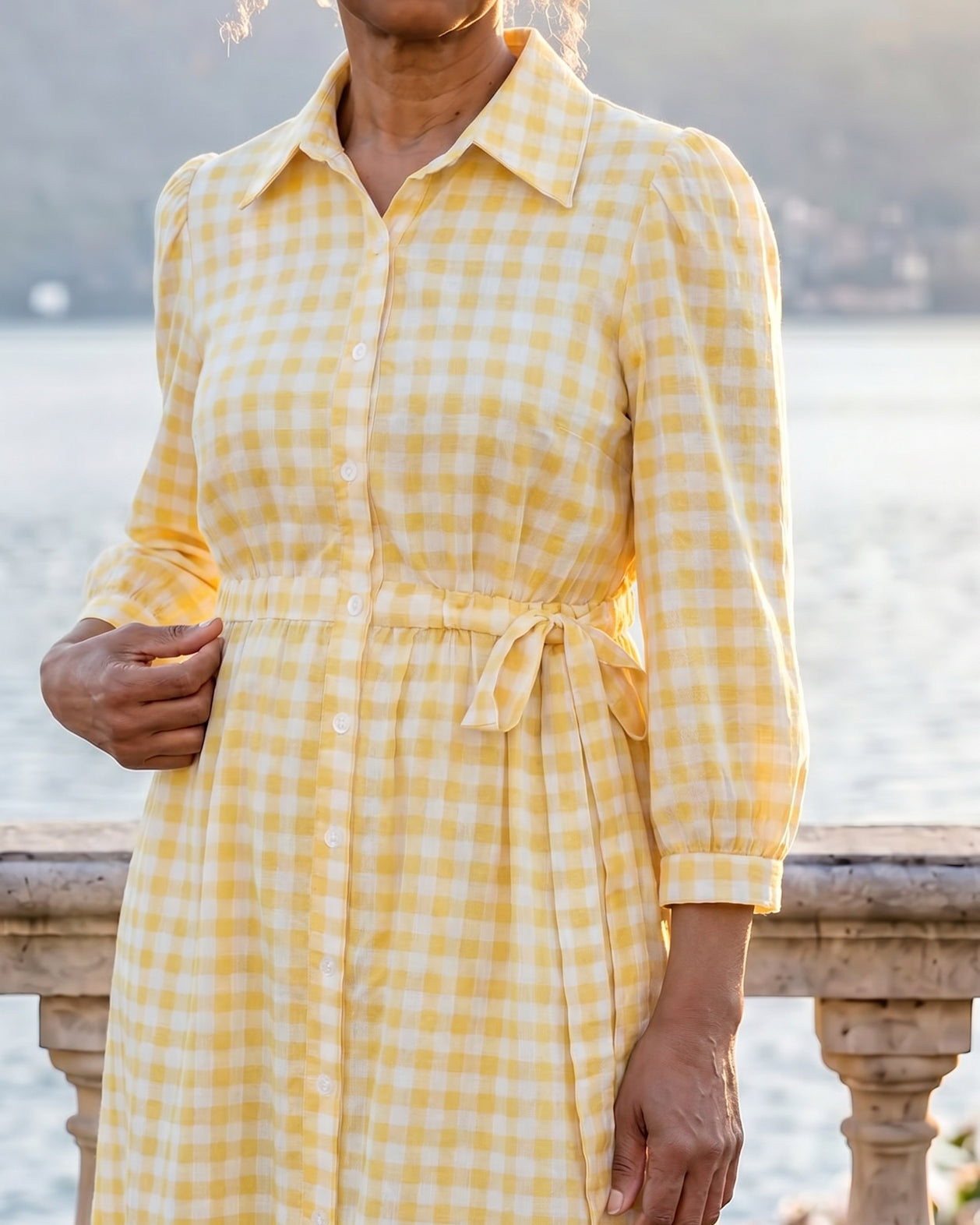 A picture of a women wearing a yellow and white gingham shirt dress with side ties.