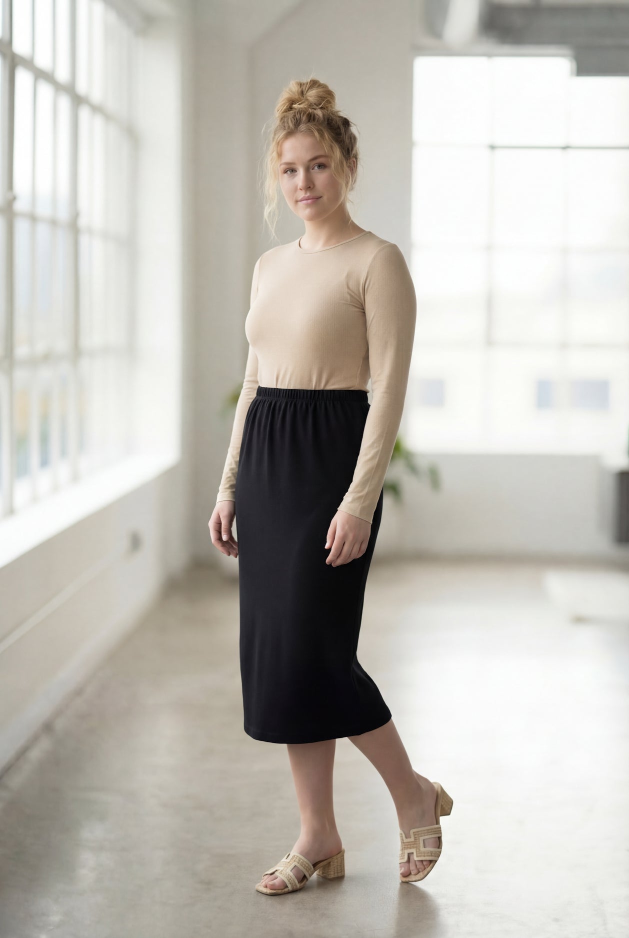 Women wearing a solid black classic 27" midi length skirt with a beige shirt in a sunlight loft.
