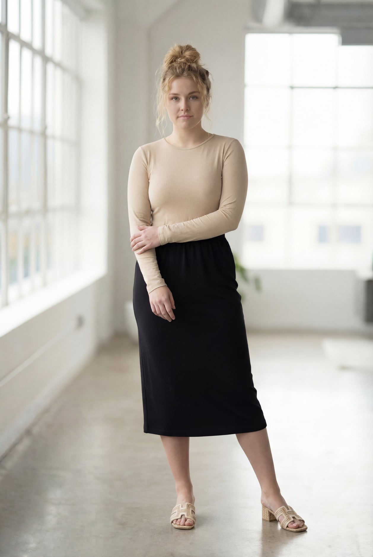 Women wearing a solid black classic 27" midi length skirt with a beige shirt in a sunlight loft.