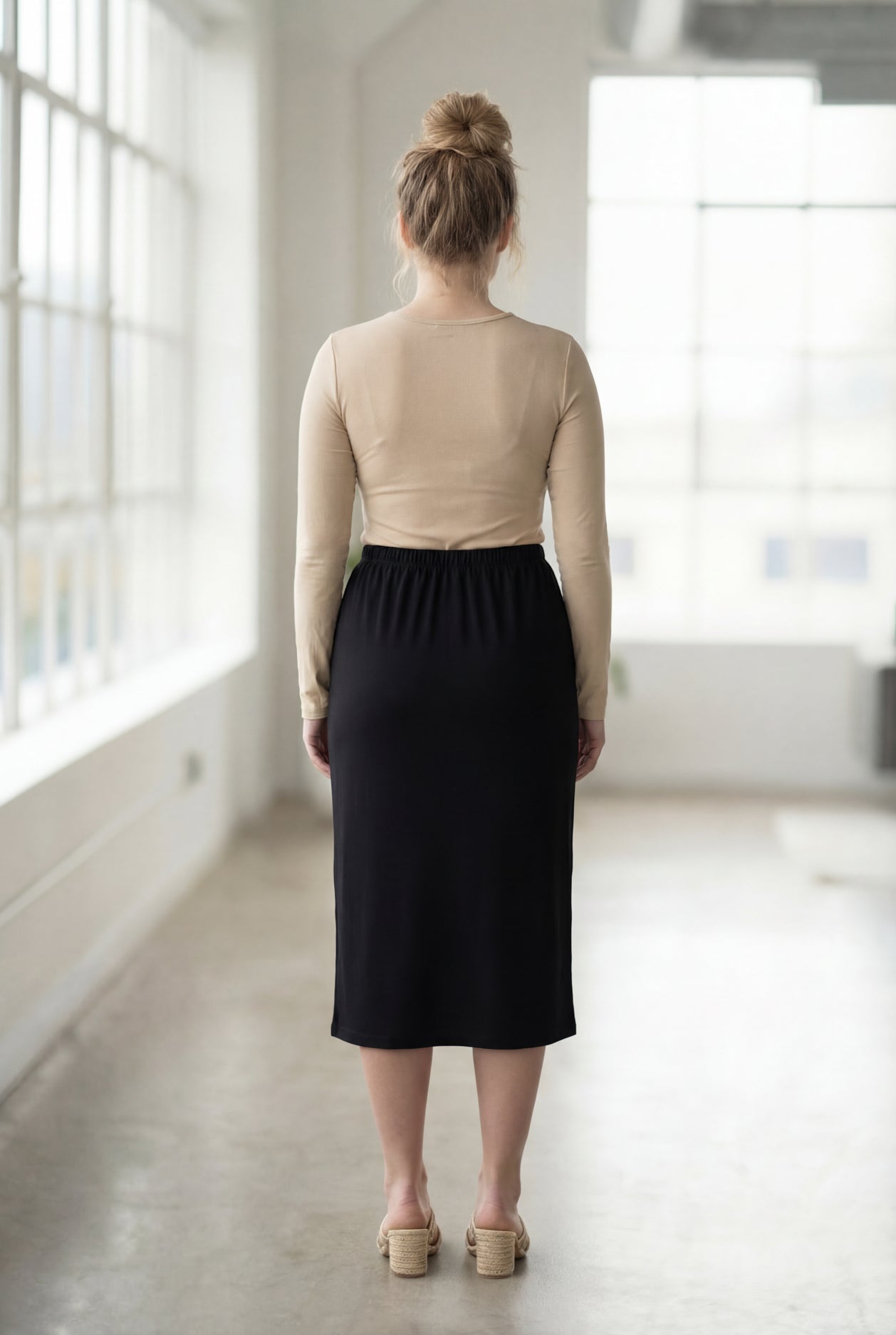 Women wearing a solid black classic 27" midi length skirt with a beige shirt in a sunlight loft.
