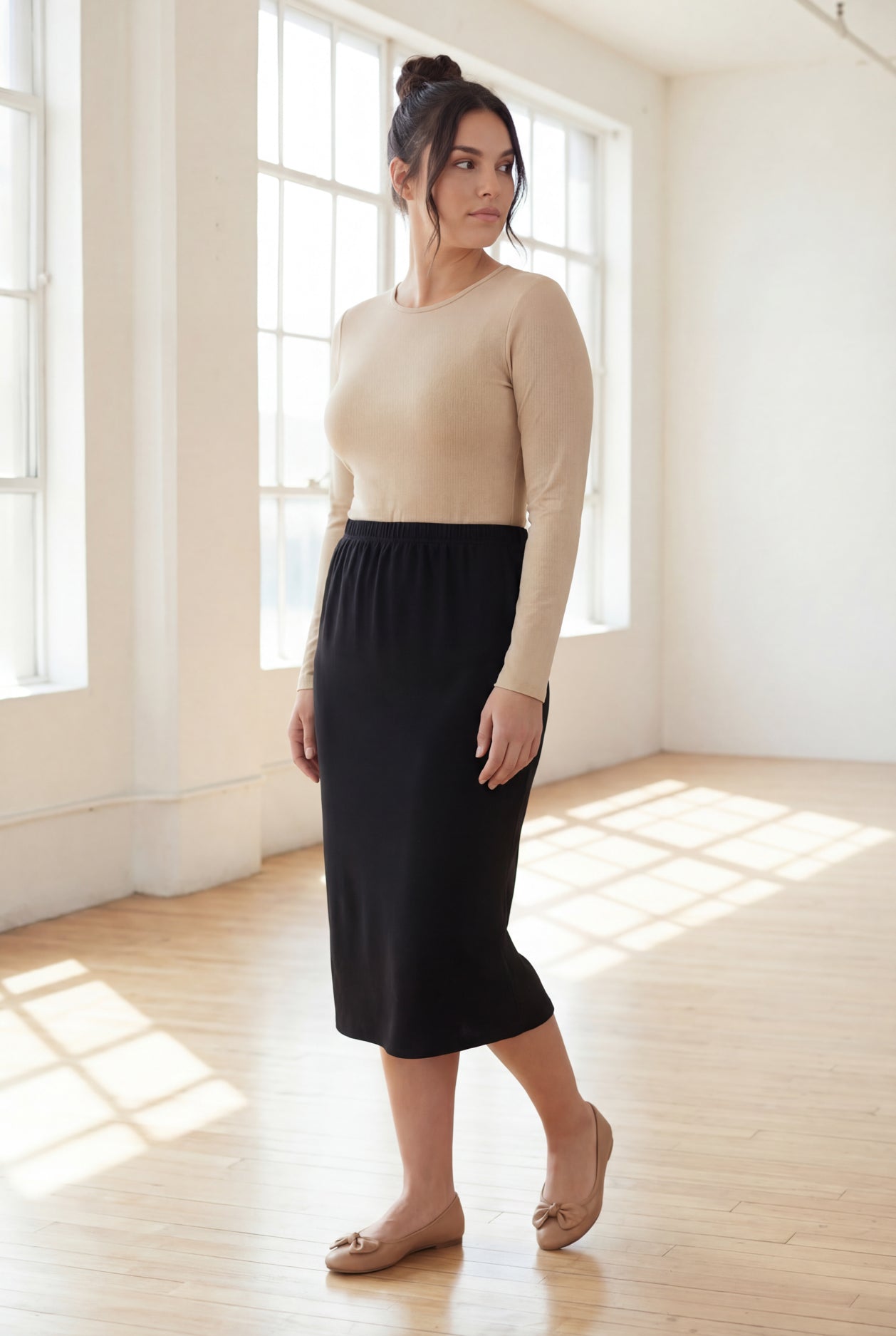 Woman wearing a beige top and black skirt in a bright room.