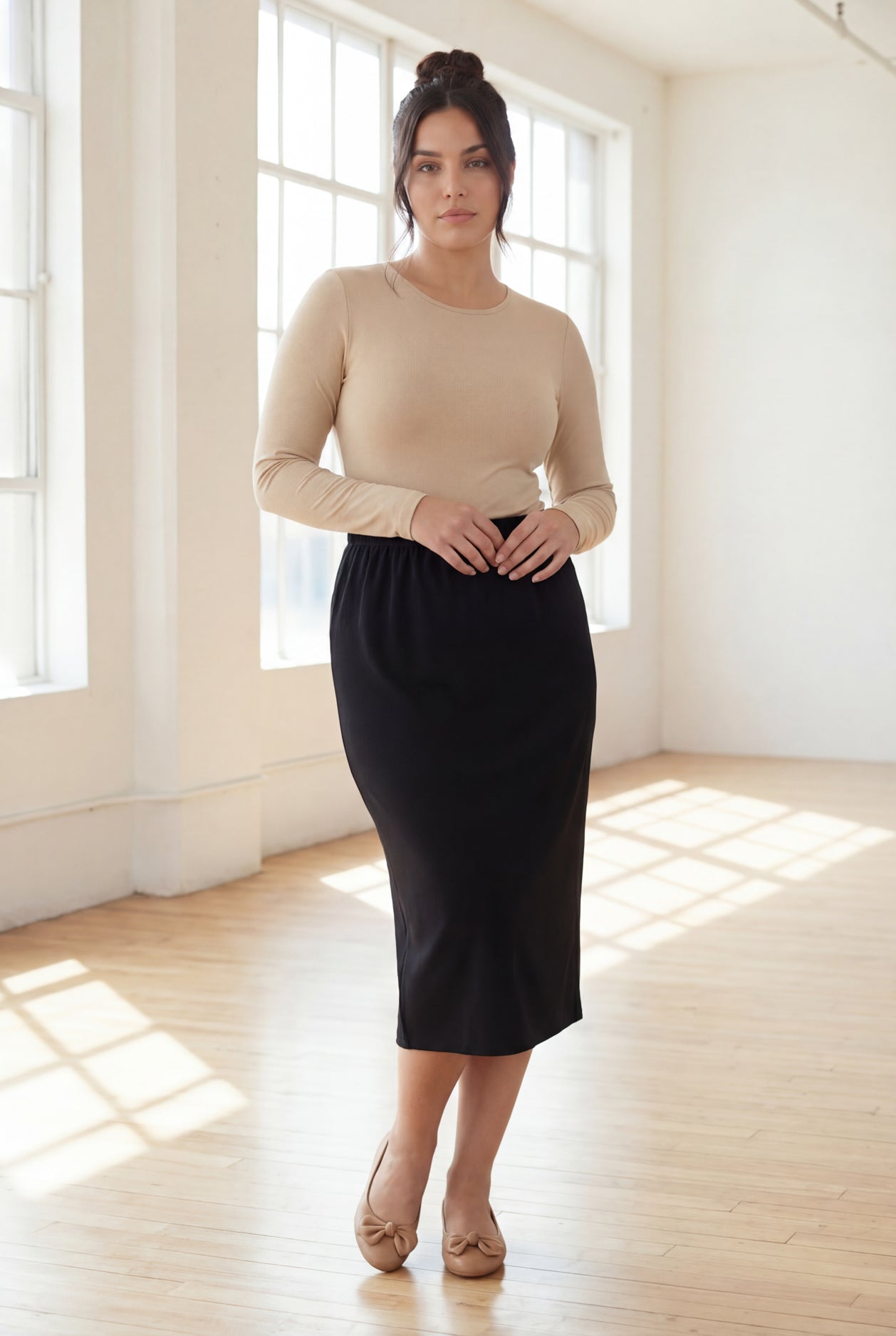 Woman wearing a beige top and black skirt in a bright room.