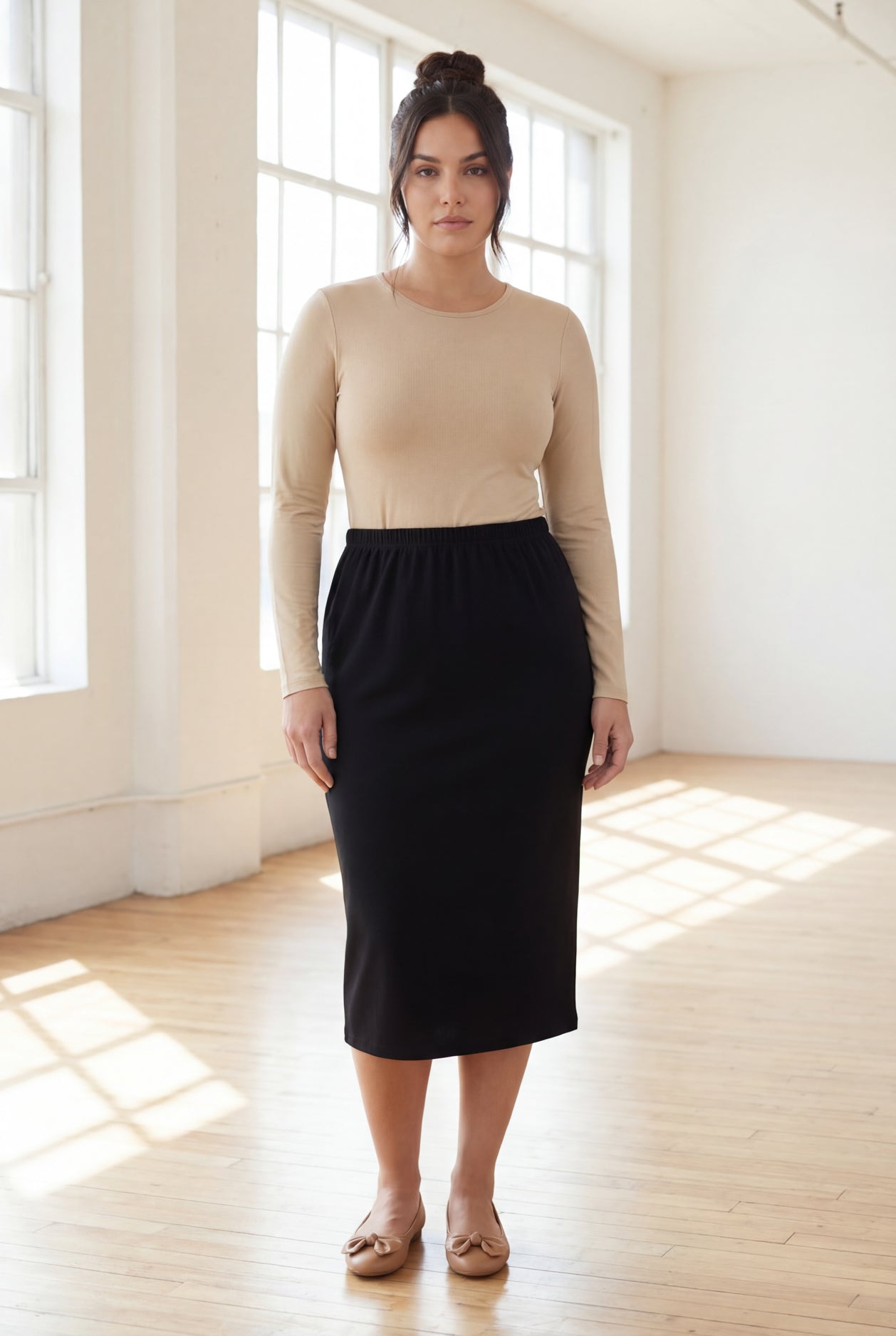 Woman wearing a beige top and black skirt in a bright room.