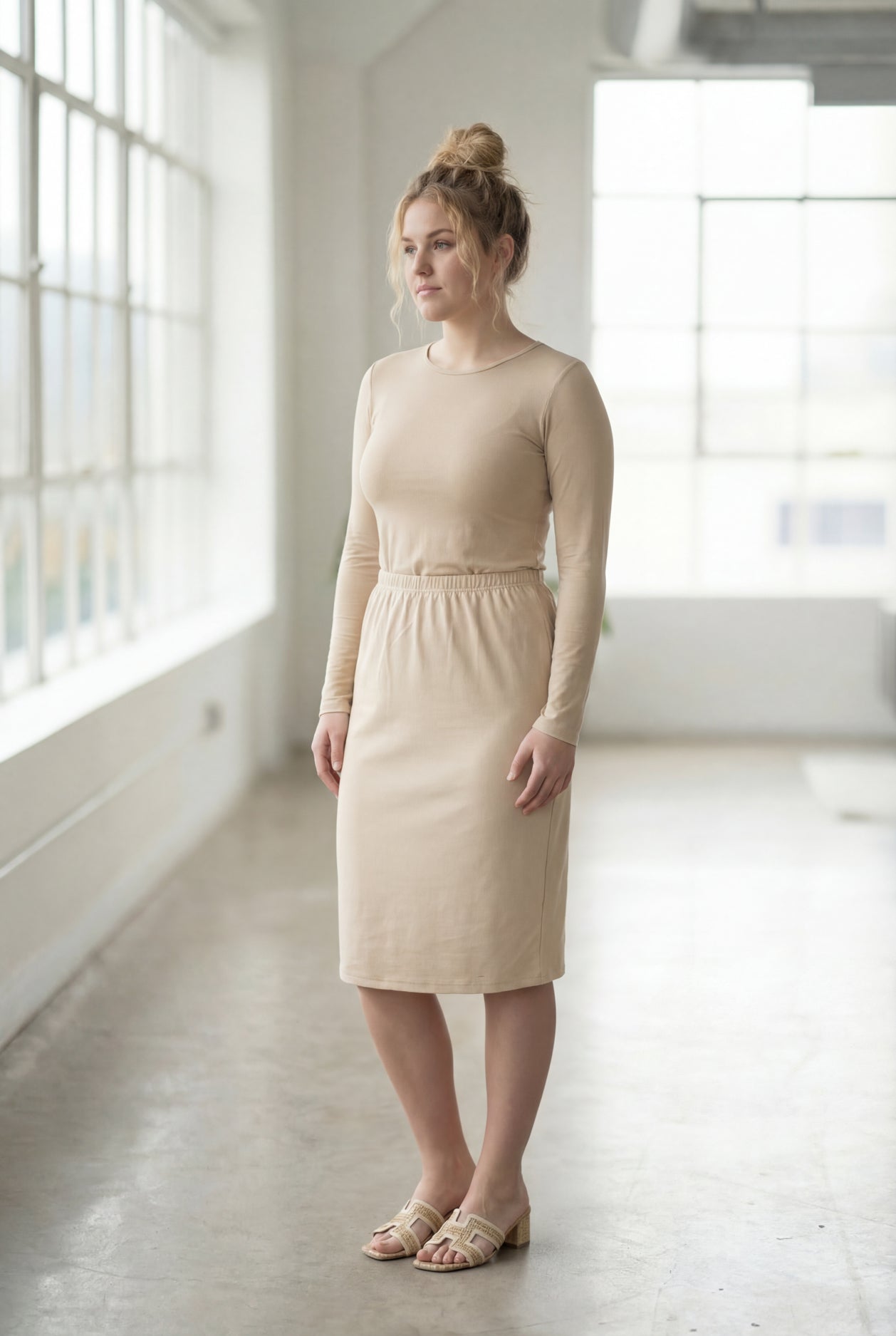 Women wearing a nude classic 27" midi length skirt with a beige shirt in a sunlight loft.