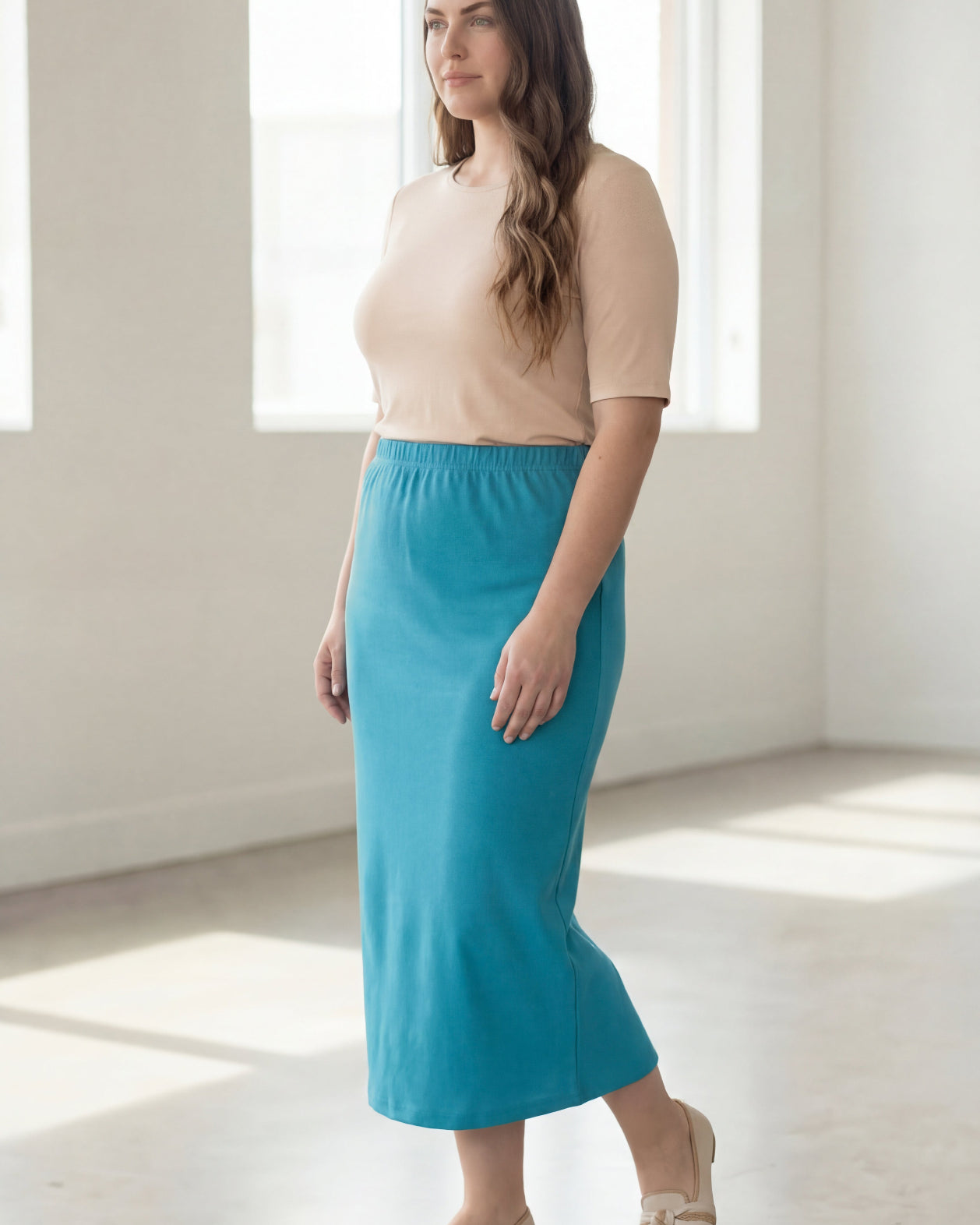 Woman wearing a beige top and blue skirt in a bright room.