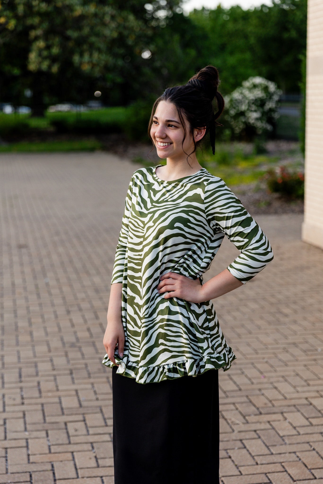Woman wearing a green and white zebra top that is generous cut with a small ruffle detail.