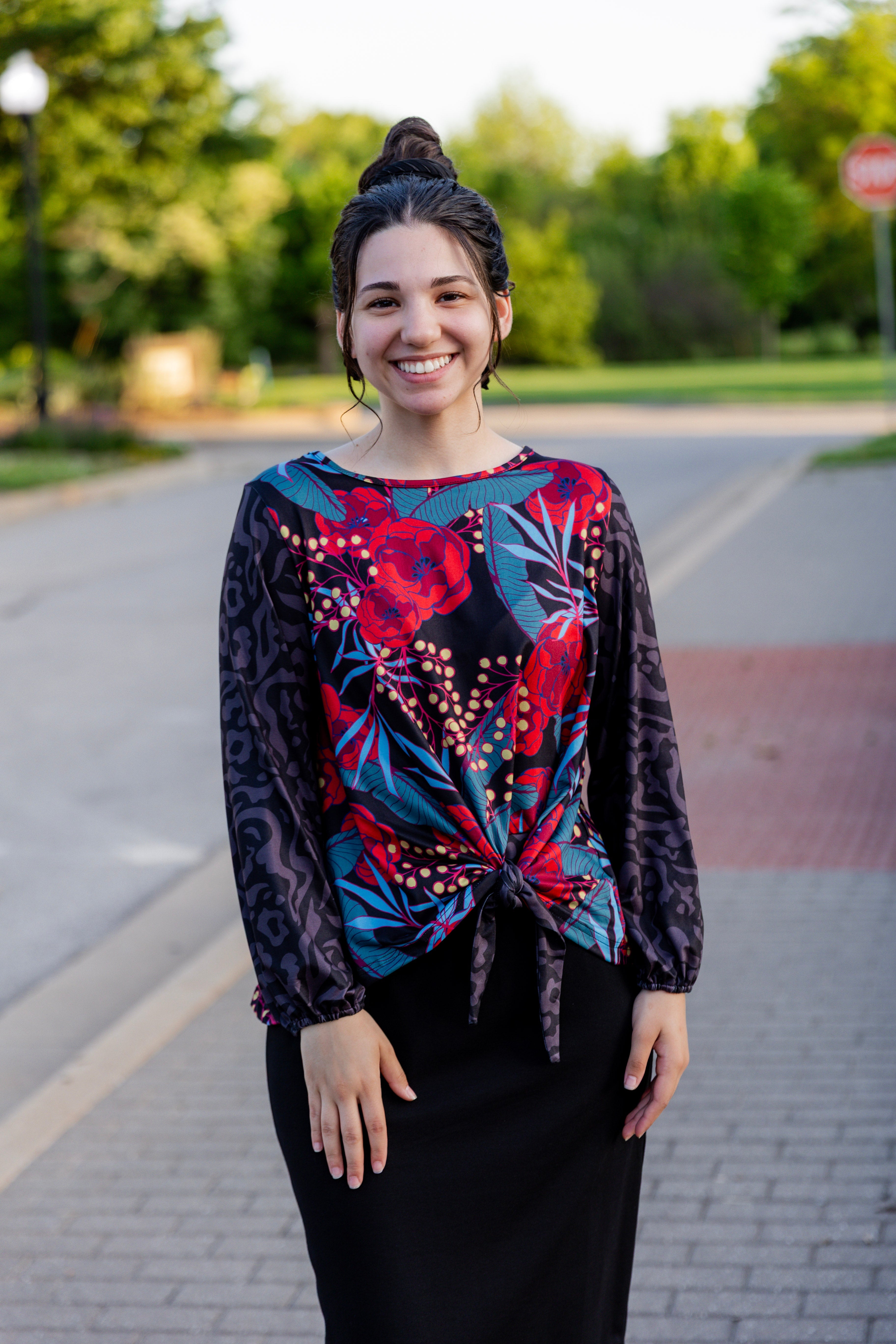 Woman wearing a modest black, red, and blue print top with a tie in the front with long sleeves.