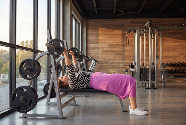  A picture of a women in a gym wearing a bight prink athletic skirt using barbells.