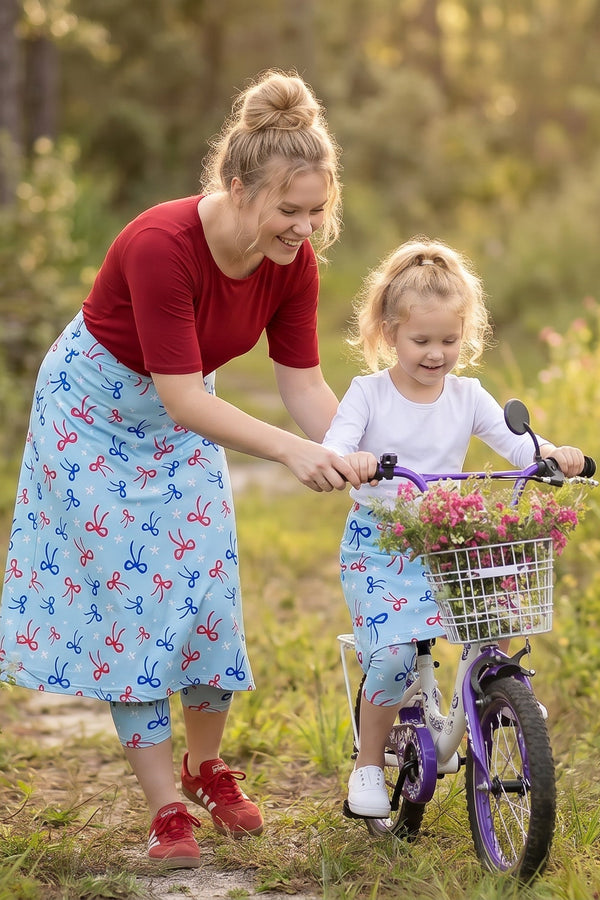 A picture of a women and girl in modest sport skirts with the girl riding a bike.